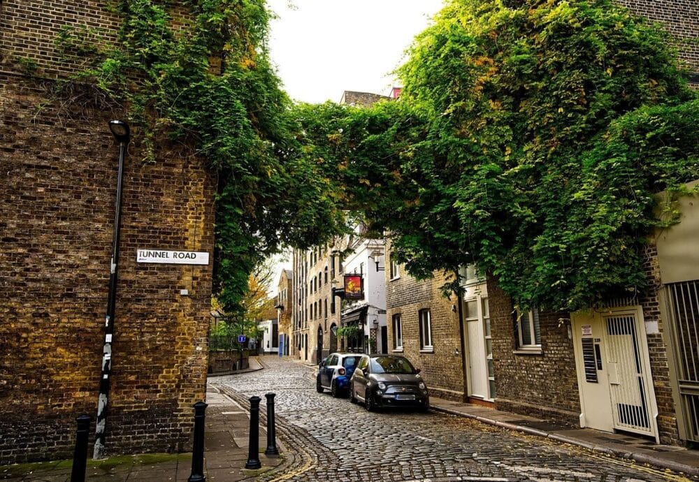A smiling man with curly hair is sitting at a desk, looking at the camera, with a laptop and a lamp in the background.