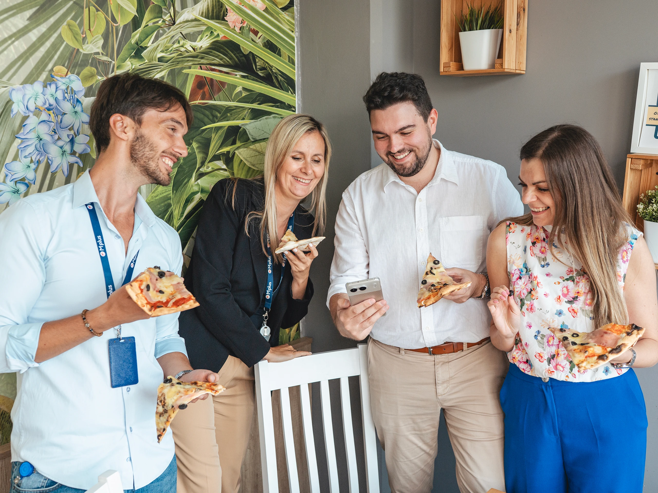 Group of colleagues enjoying pizza and laughing during an office break.