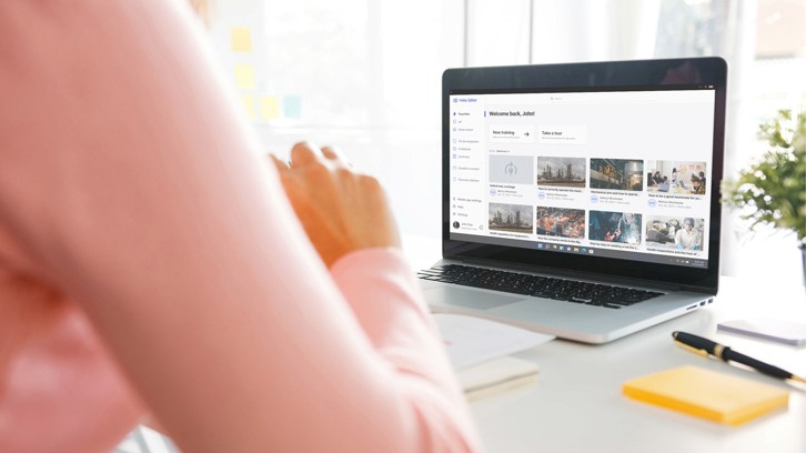 A talent recruiter with a soft smile working on her laptop in the office. The angle is on her face so we can't see what's is on the screen. She is wearing a blazer 