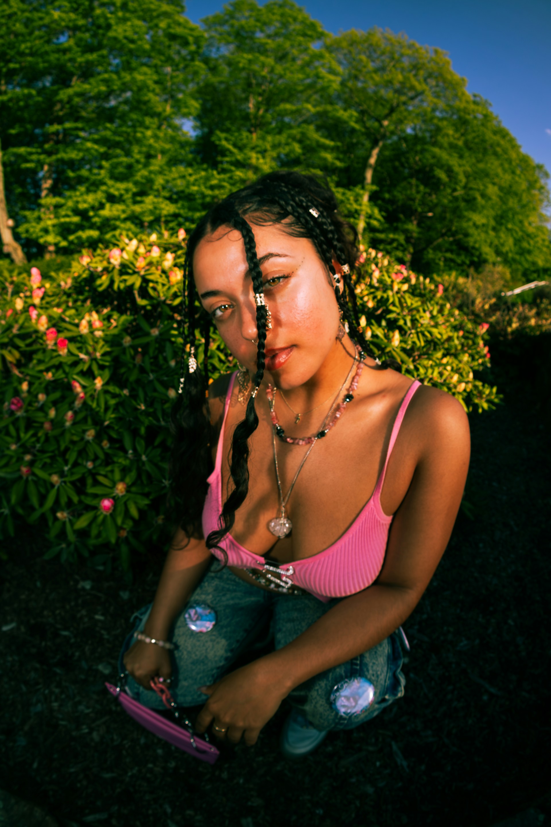 High-angle fish-eye portrait of a woman in a pink top near flowering bushes.