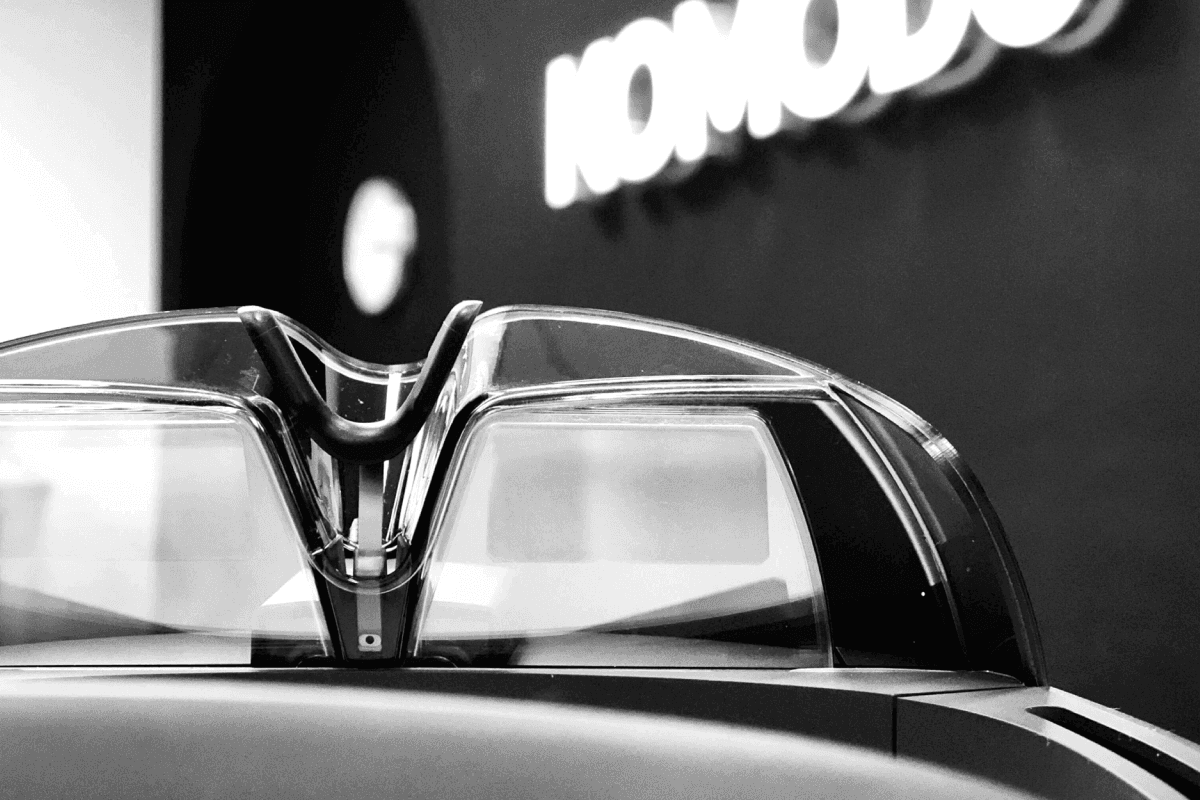 Black and white image of a zoomed in AR glasess, with the KOMODO logo wall in the background