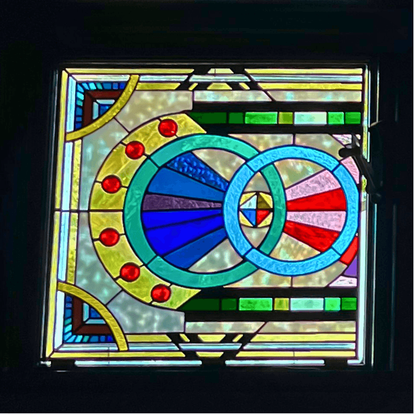 Art Deco stained-glass window with intersecting turquoise circles, colored rays, and a black frame
