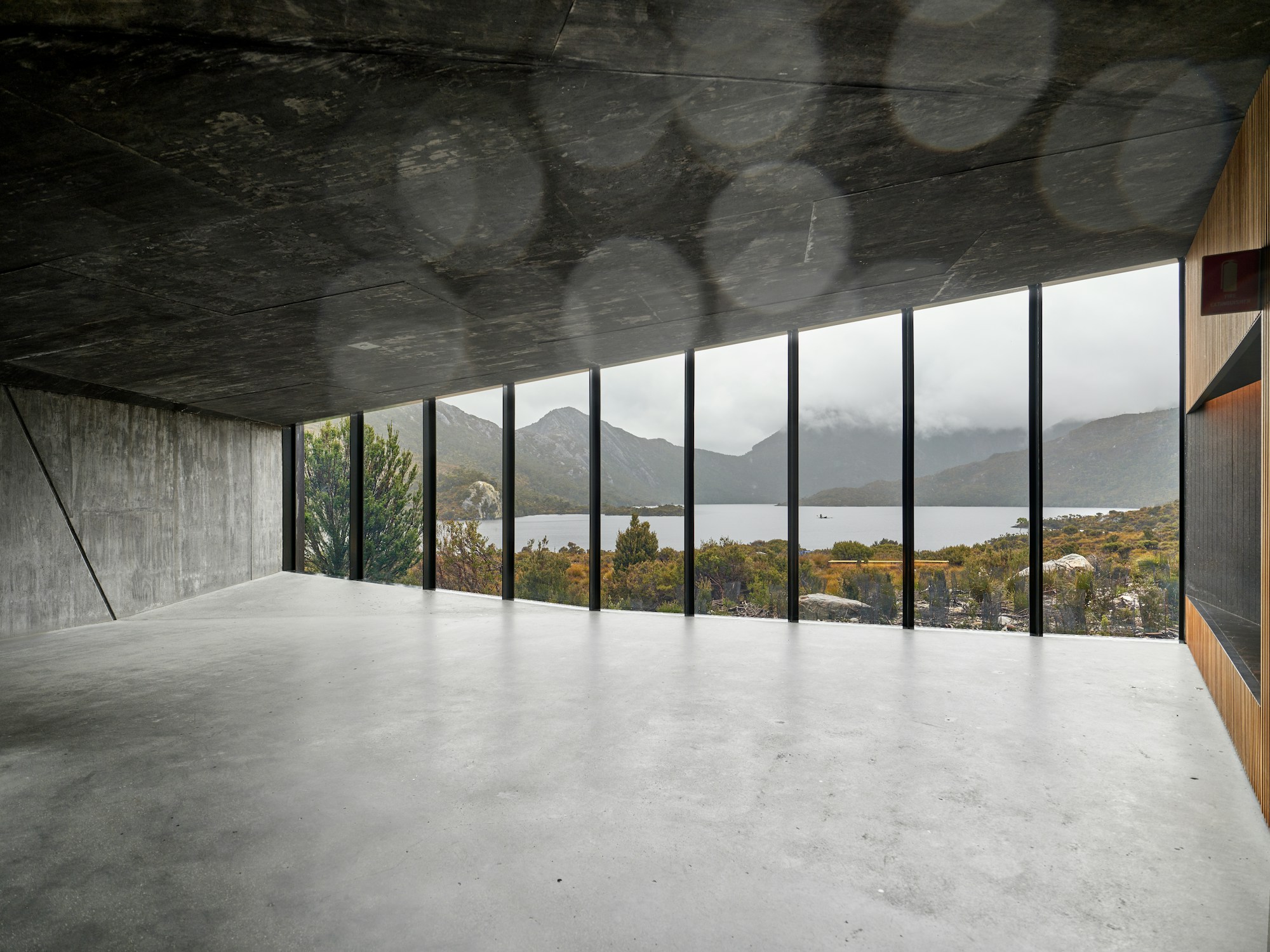 Open concrete room with a full-height glazed wall framing the lake