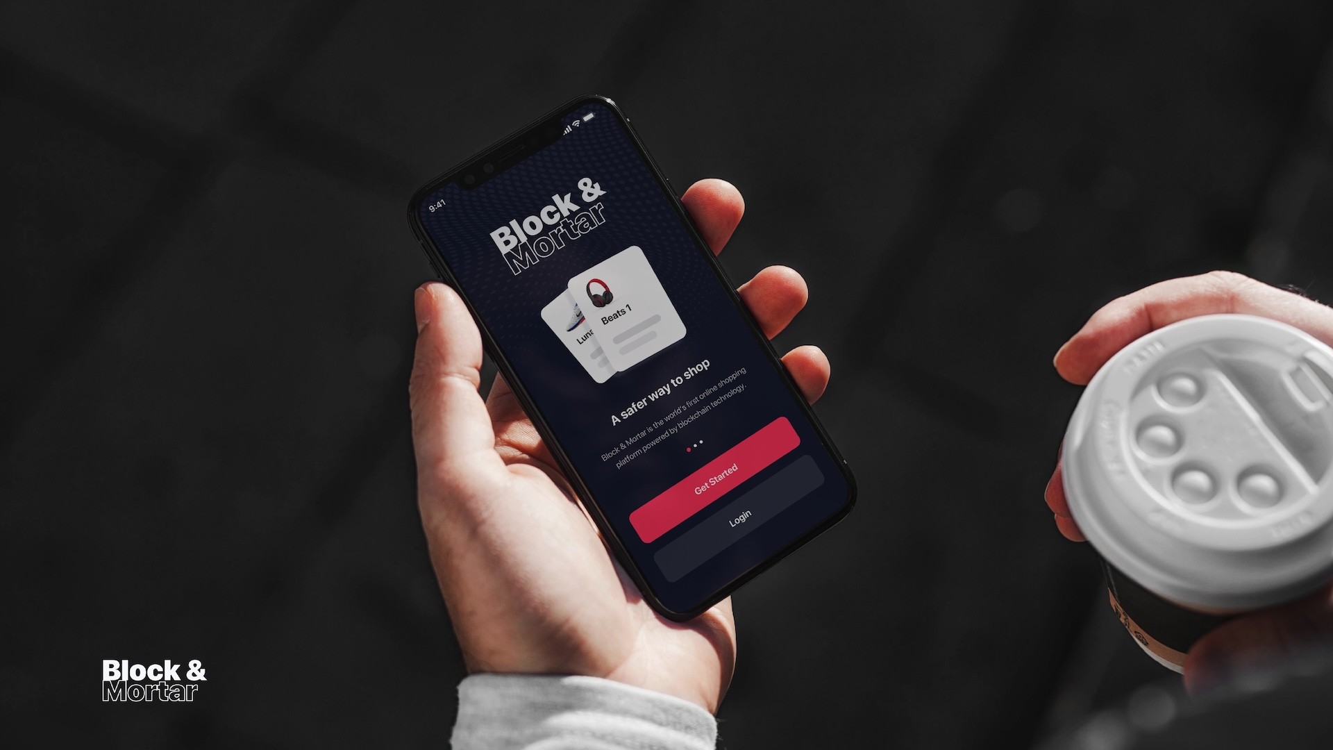 Lifestyle mockup of Block & Mortar mobile app welcome screen held in hand with coffee cup, showing dark UI with product cards, "A safer way to shop" messaging, and pink call-to-action buttons for blockchain e-commerce platform onboarding