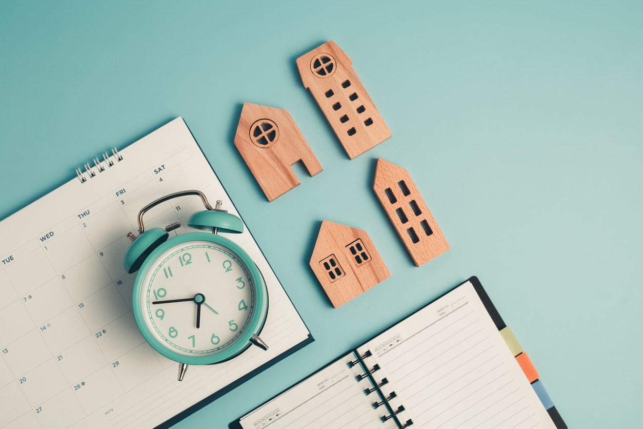 Wooden houses, alarm clock, and calendar on blue background.