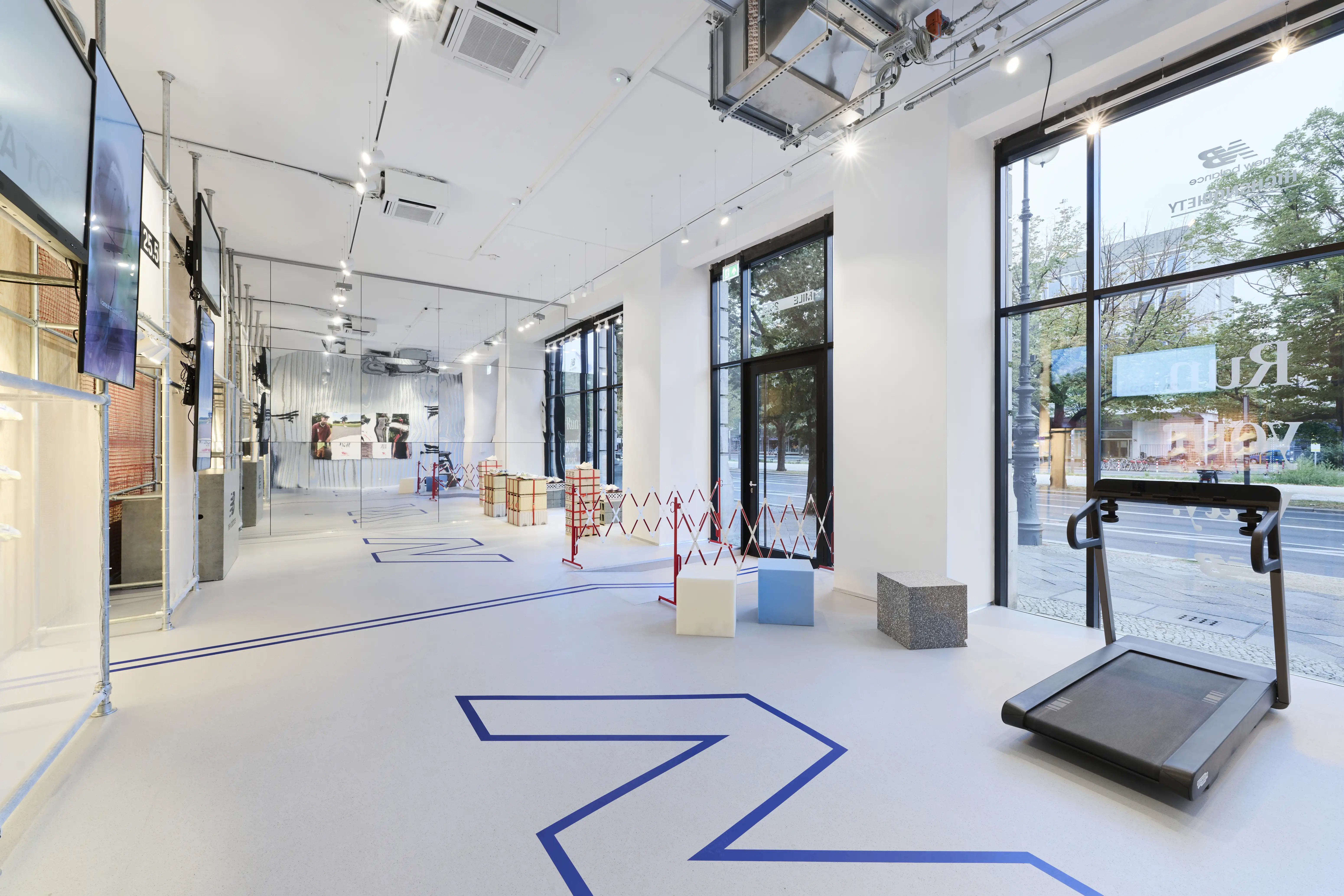 Bright pop-up space with treadmill, blue zigzag floor line and construction-site barriers at Highsnobiety x New Balance.