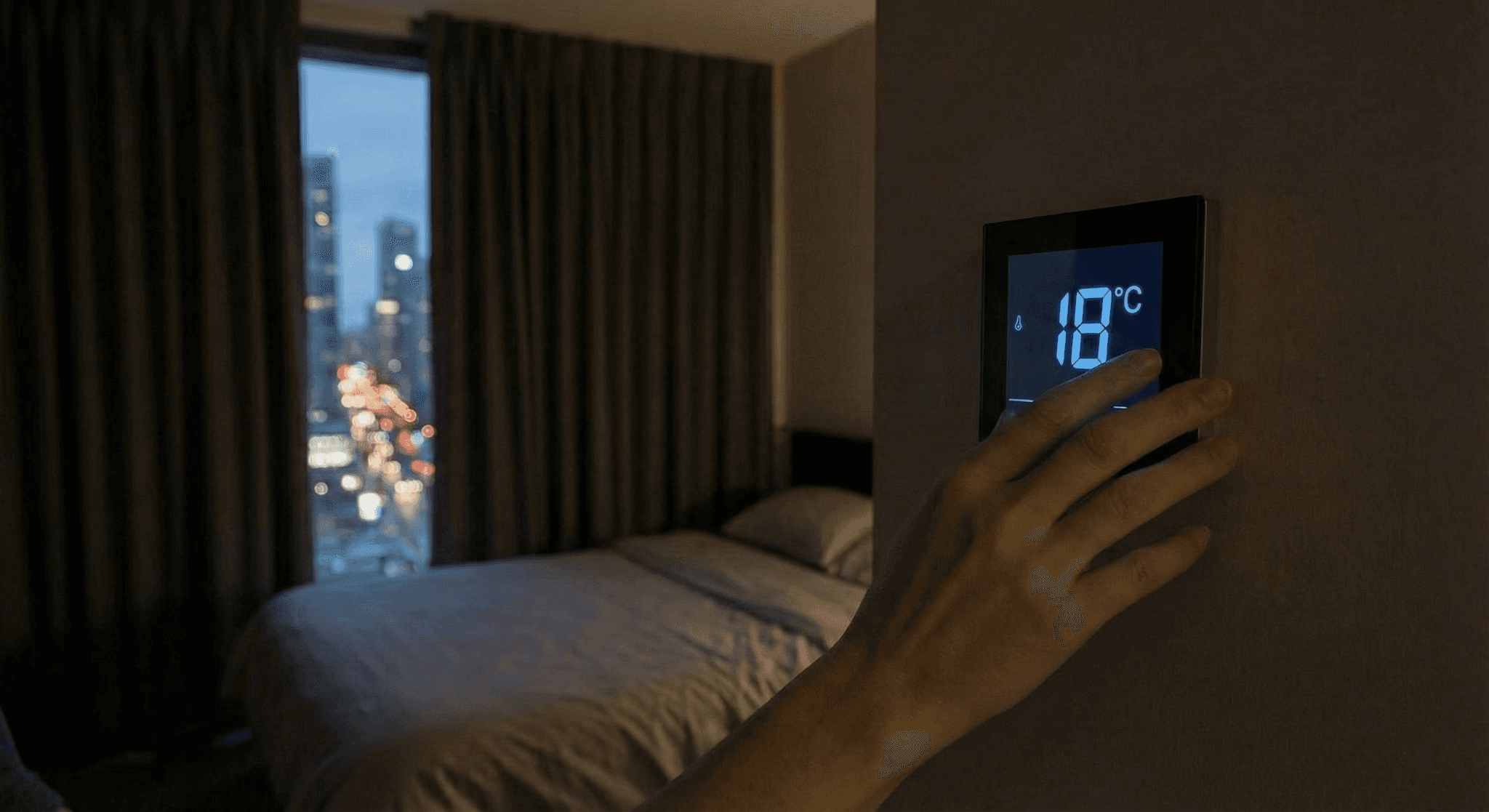 Hand adjusting a wall thermostat to 18°C in a dim bedroom at night