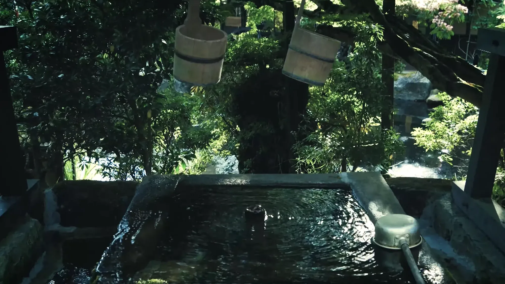 An open-air bath at Kurokawa Onsen at dusk under hanging lamps, greenery close around the water