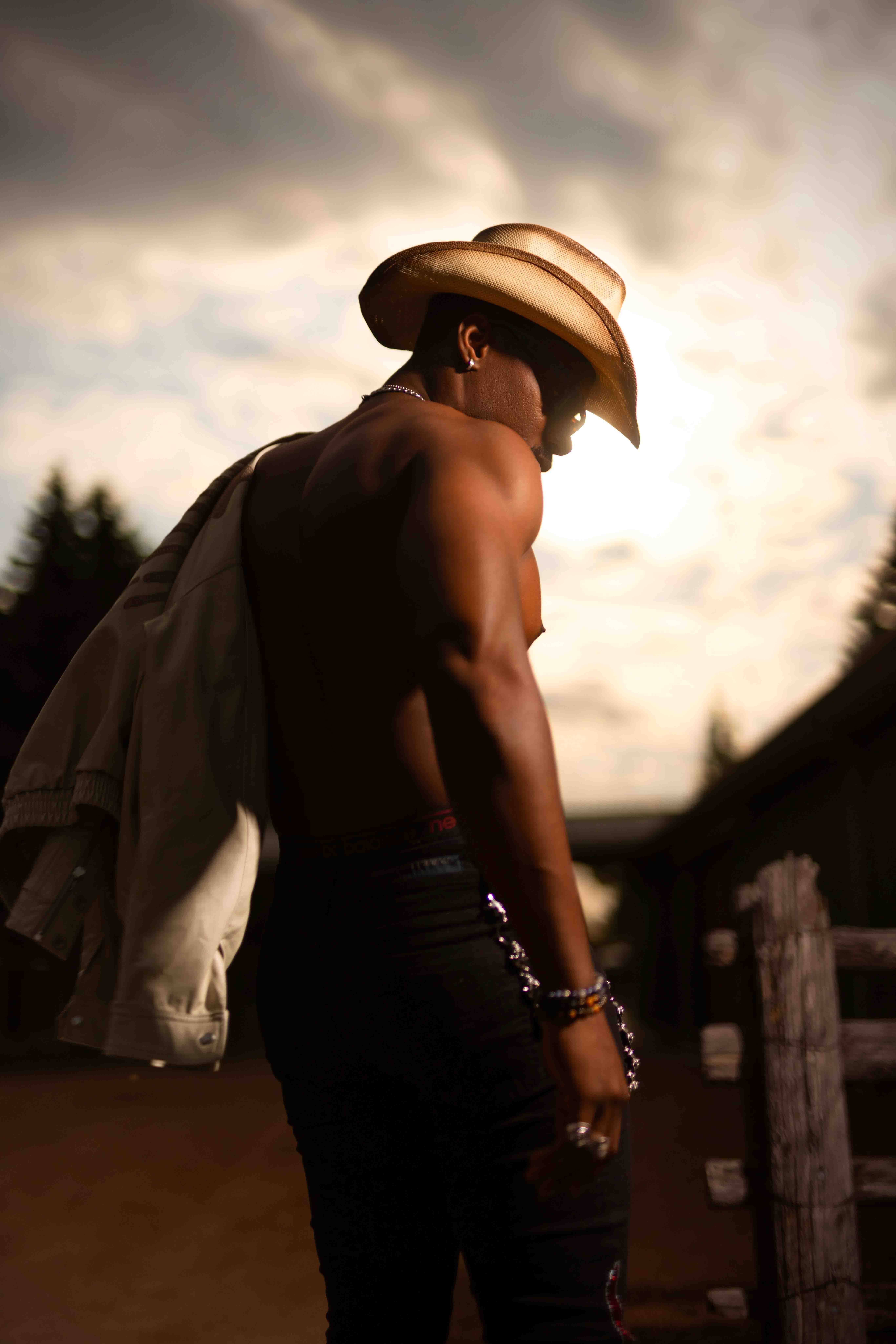 Person in a cowboy hat at sunset, leaning on a fence