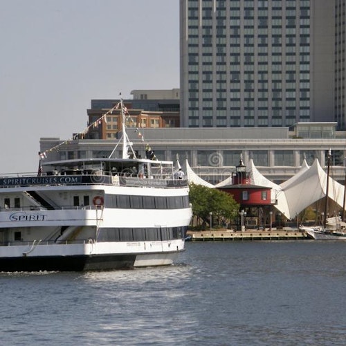 A large white cruise ship named "Spirit" near a waterfront with buildings, including a canopy-covered structure, in the background.