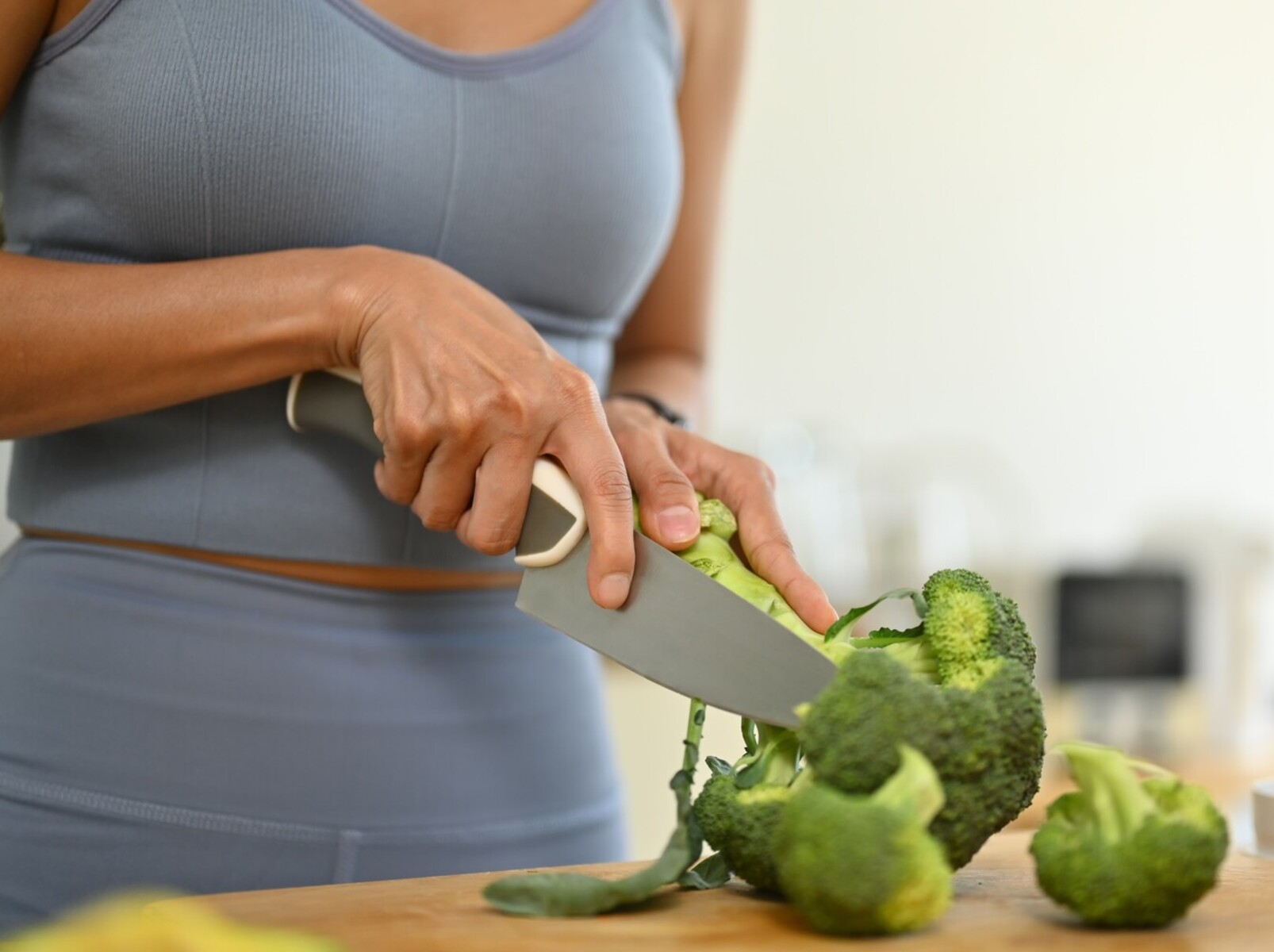 woman chopping broccoli to prepare a healthy meal to eat after her treadmill routine to lose weight