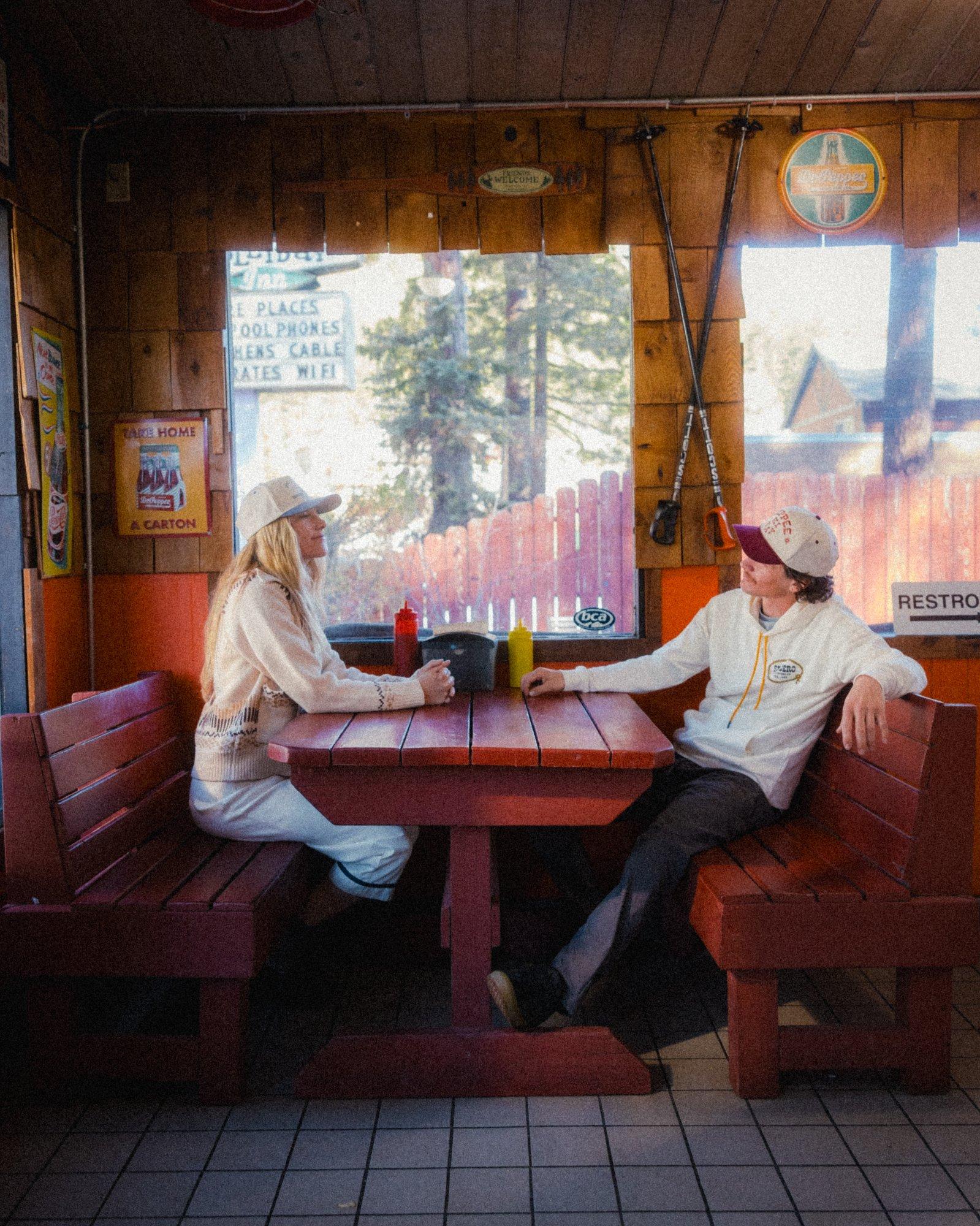 A man and woman sitting in a cabin diner at a red table