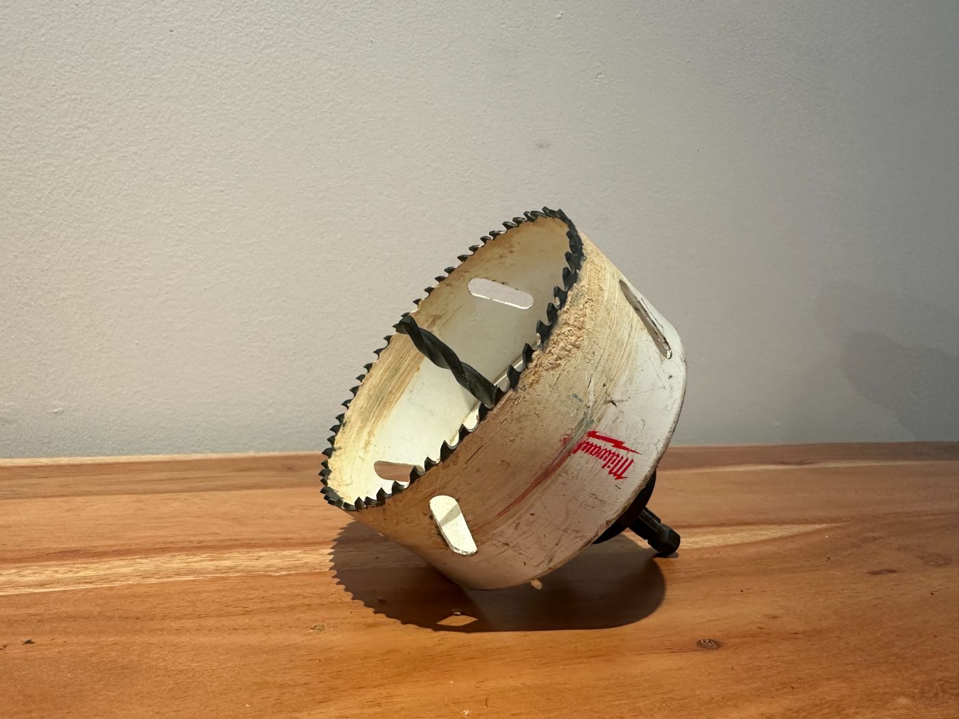 Scie cloche Milwaukee de 4 pouces avec foret central, posée sur une surface en bois, outil utilisé pour percer de larges ouvertures dans le bois ou le plâtre