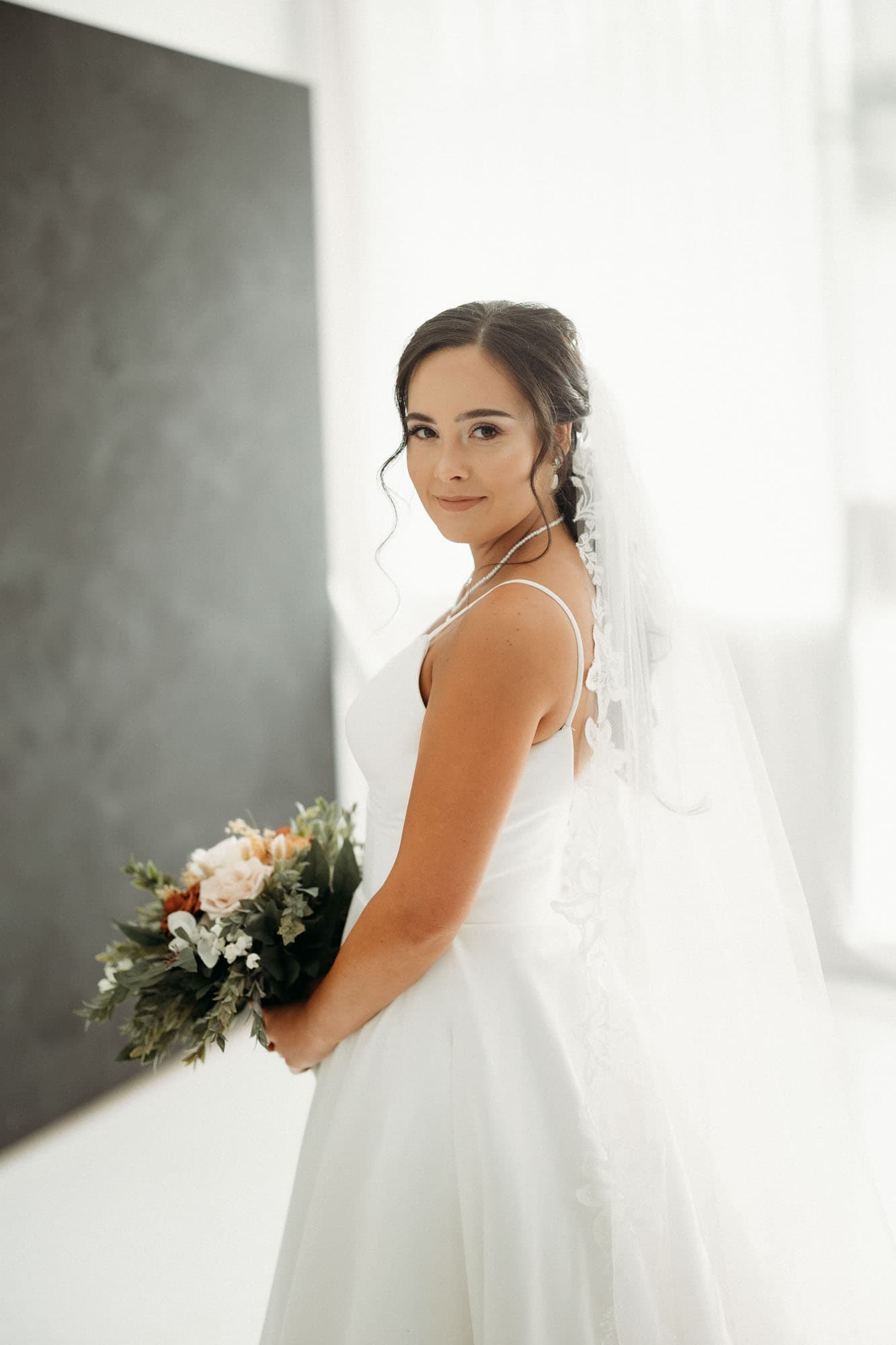 A bride poses with her bouquet in hand, her veil flowing behind her, in a naturally lit bridal session at Revelator Studio, a photography studio in Shreveport.