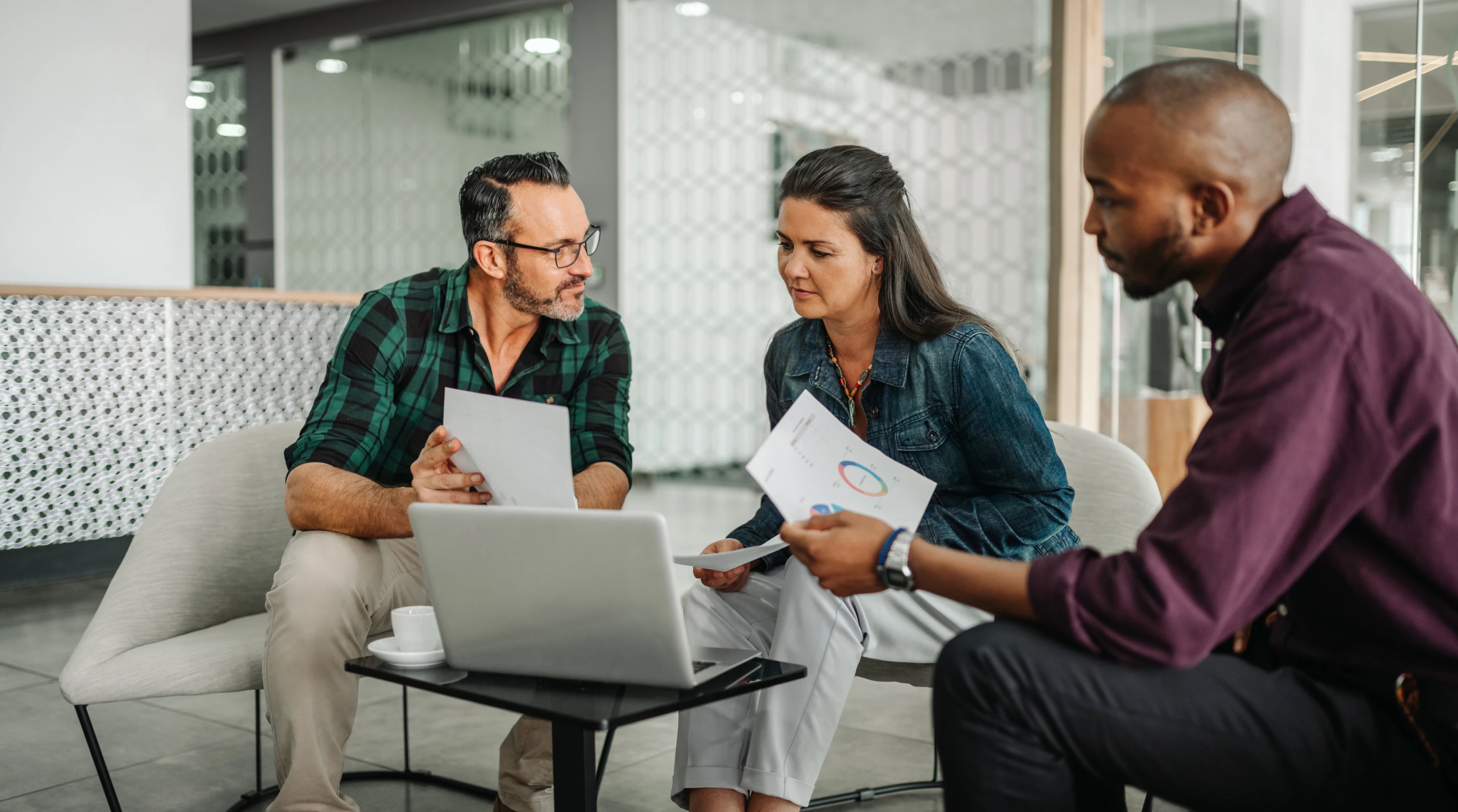 3 people sat together looking at paper and laptop