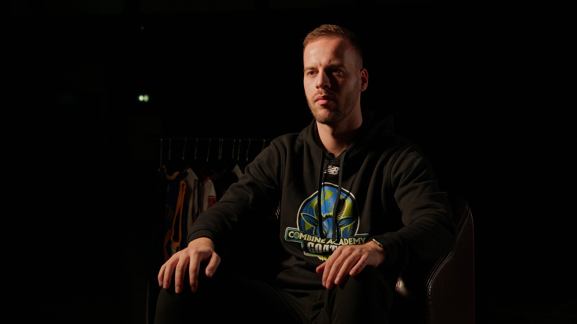 Portrait d’un coach de la Combine Academy assis dans un fauteuil, en lumière tamisée.