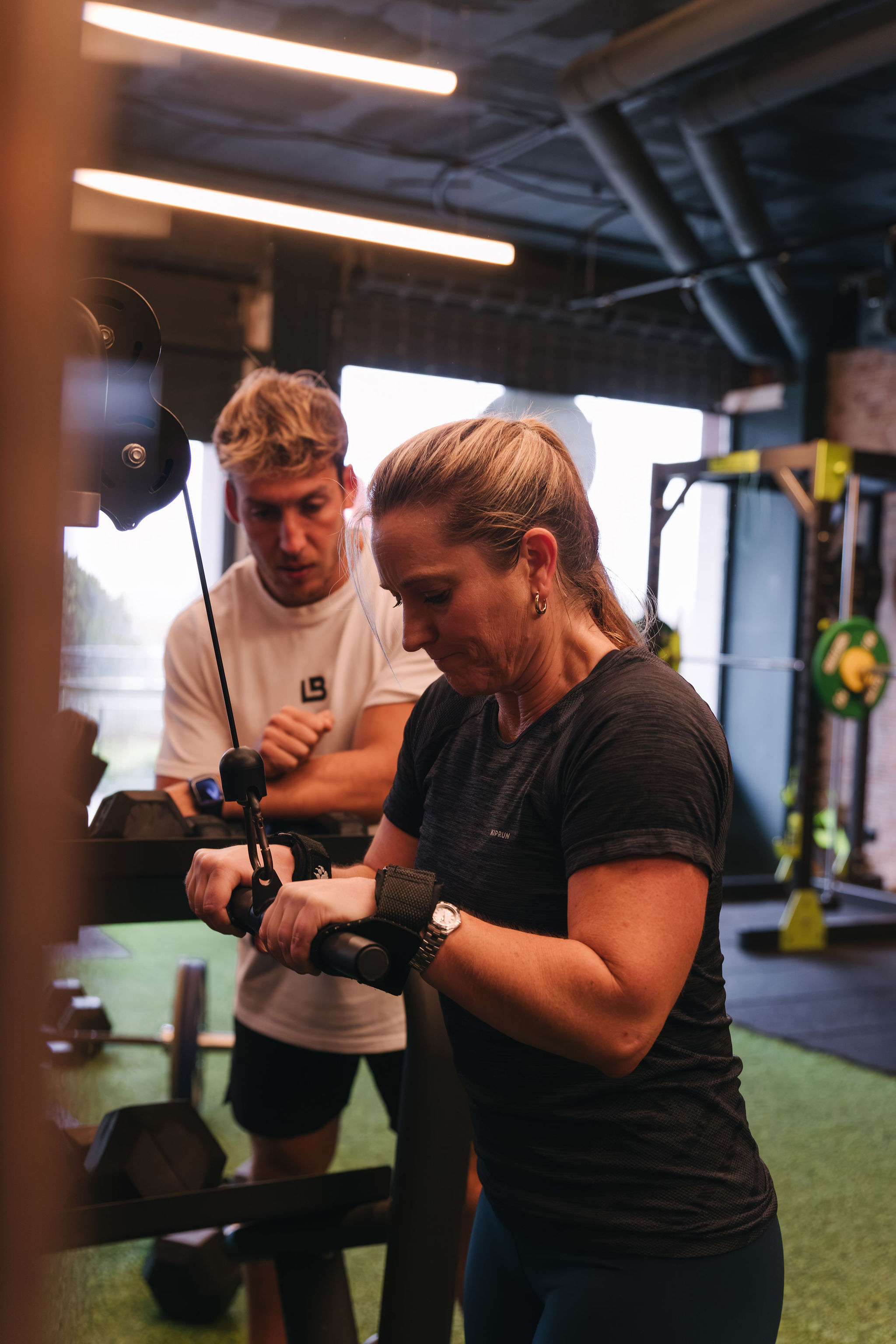 Cliente realizando ejercicio en polea con supervisión de entrenador en La Base Strength, Sitges