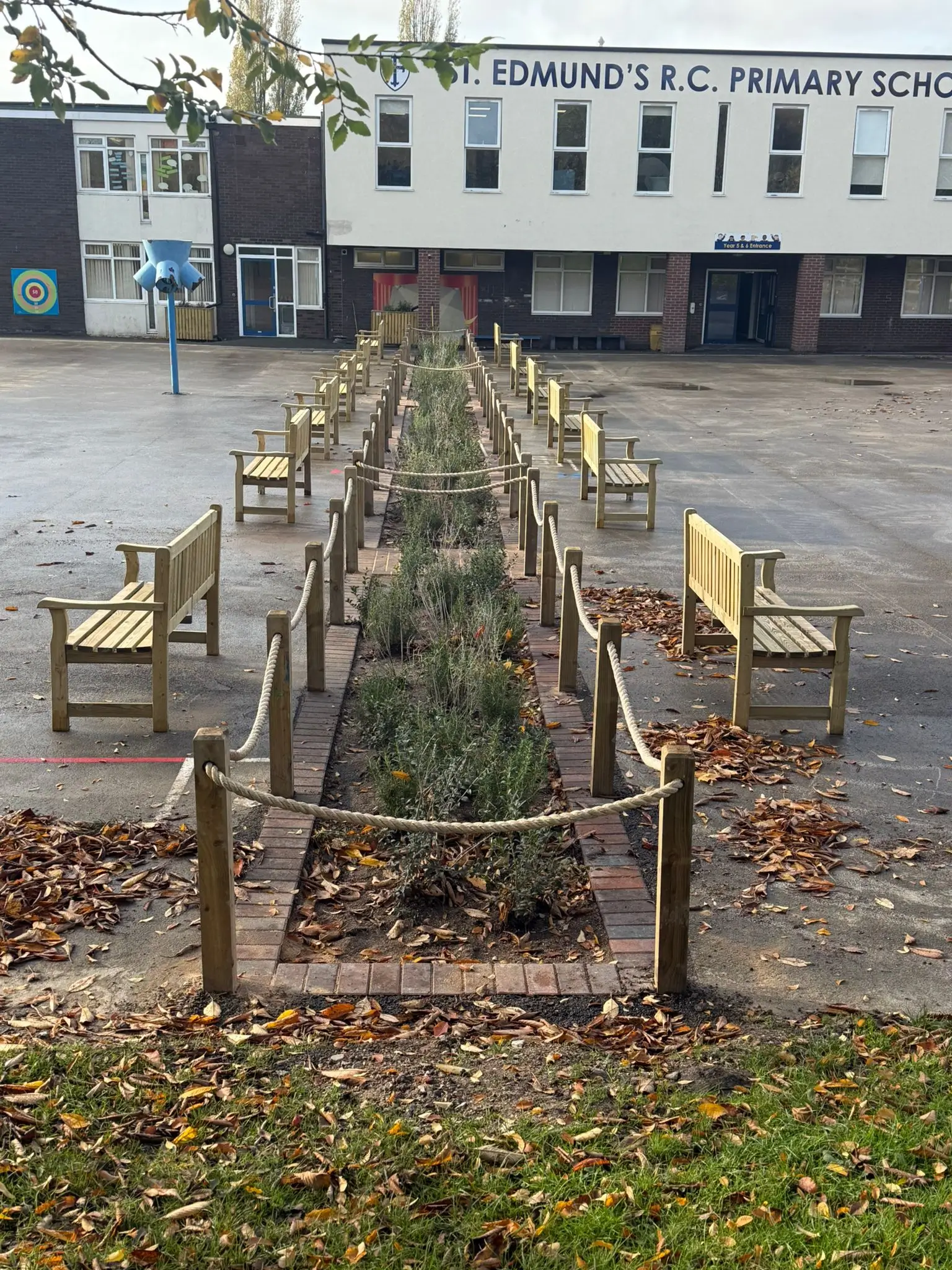 A raised garden bed with wooden frames and benches, set against a building in an open area.