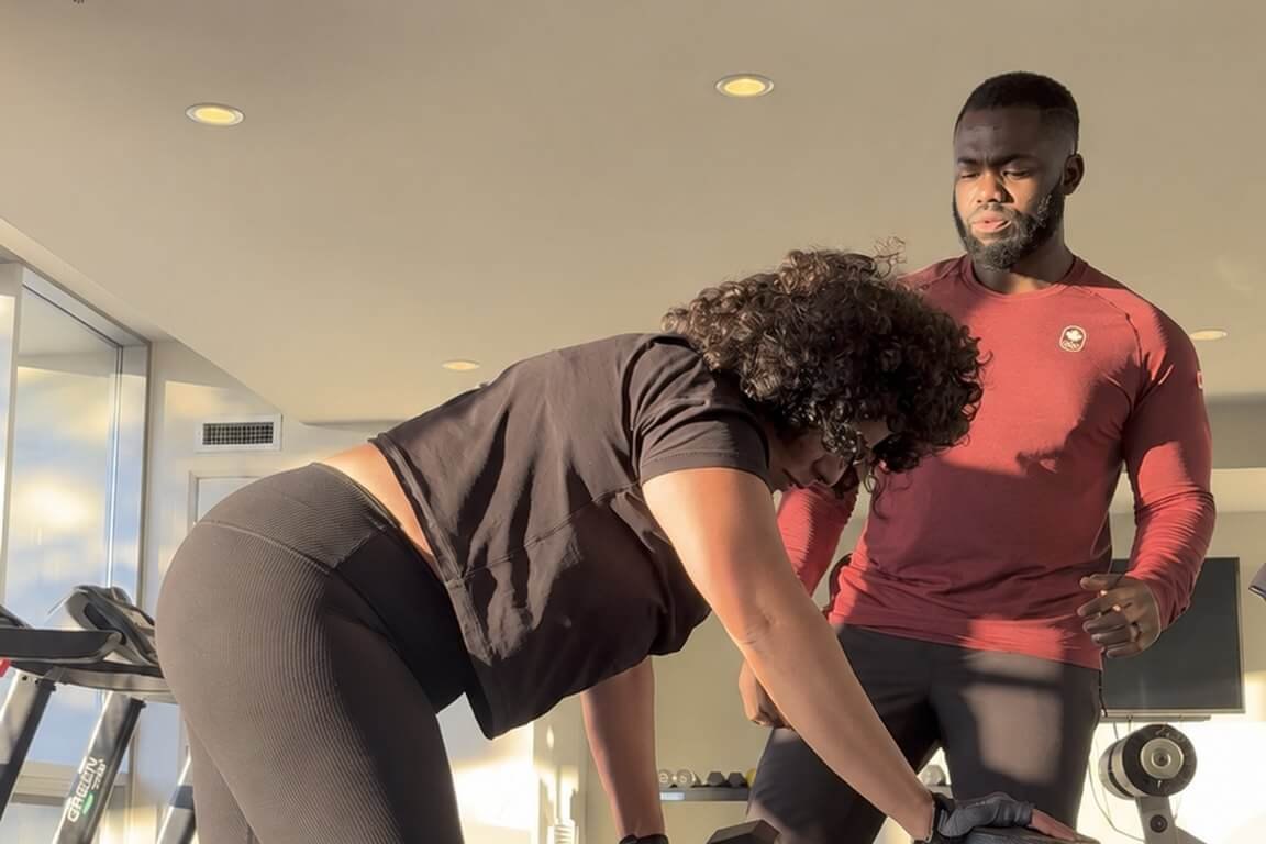 Doug Koomson coaching a client through a dumbbell row in a sunlit gym