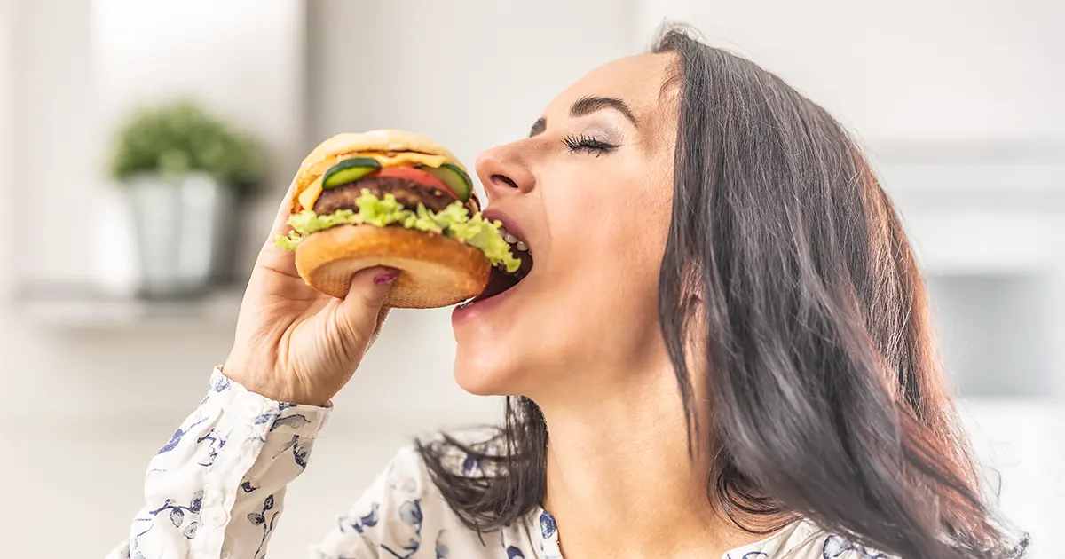 Illustrasjonsbilde av en ung kvinne som spiser hamburger.