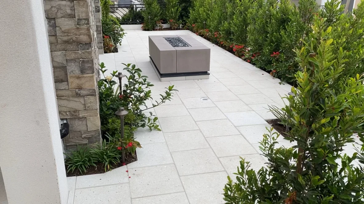 Paved patio and side path beside planted borders and a fire table.