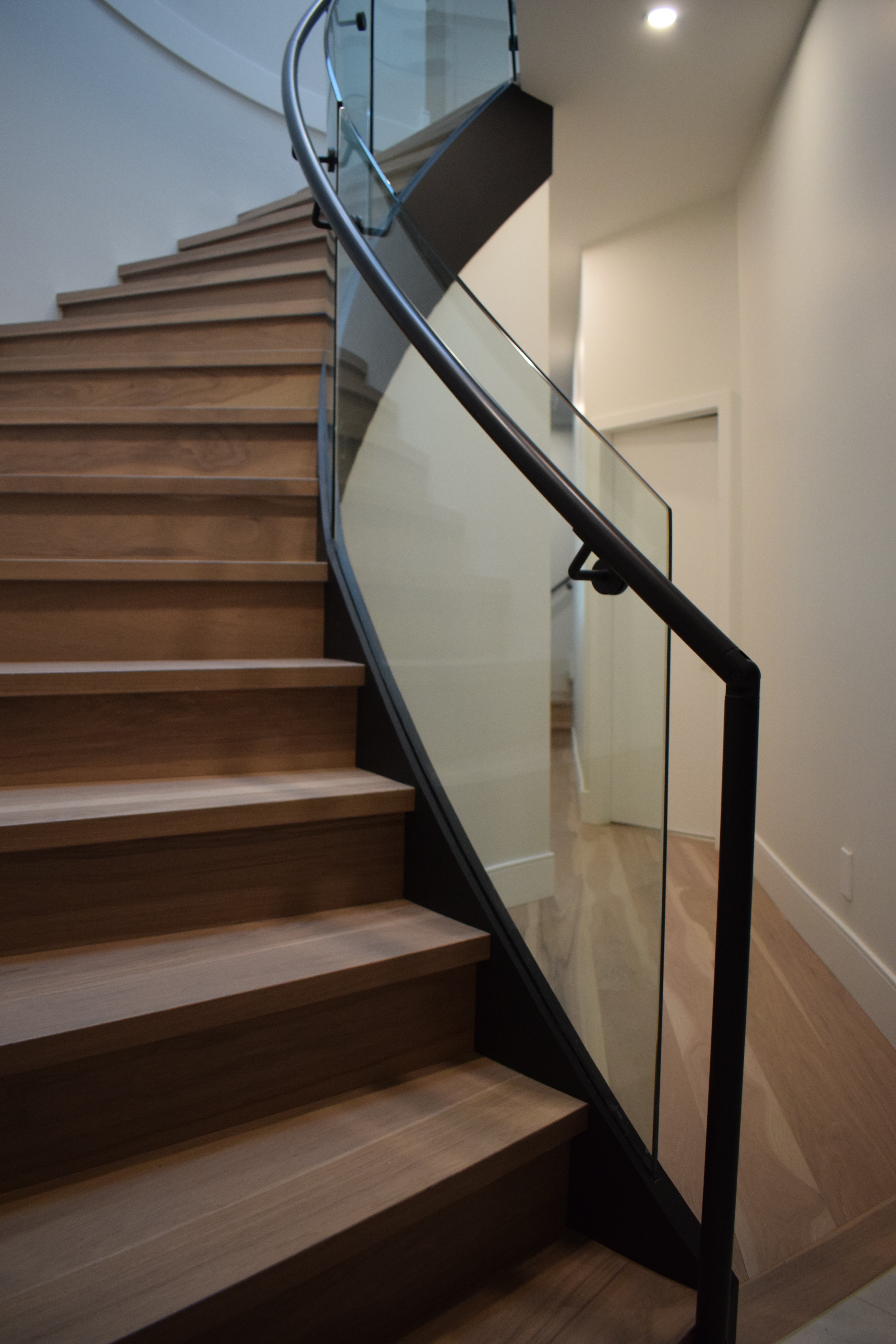 Custom curved glass railing with black handrail on a wood interior staircase