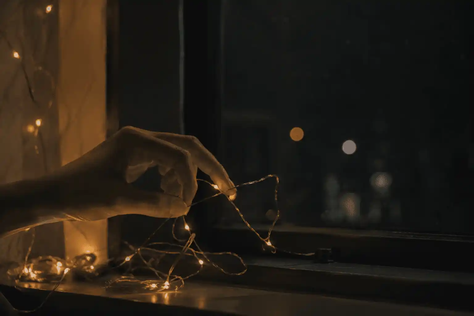 A hand reaching toward a delicate strand of warm lights