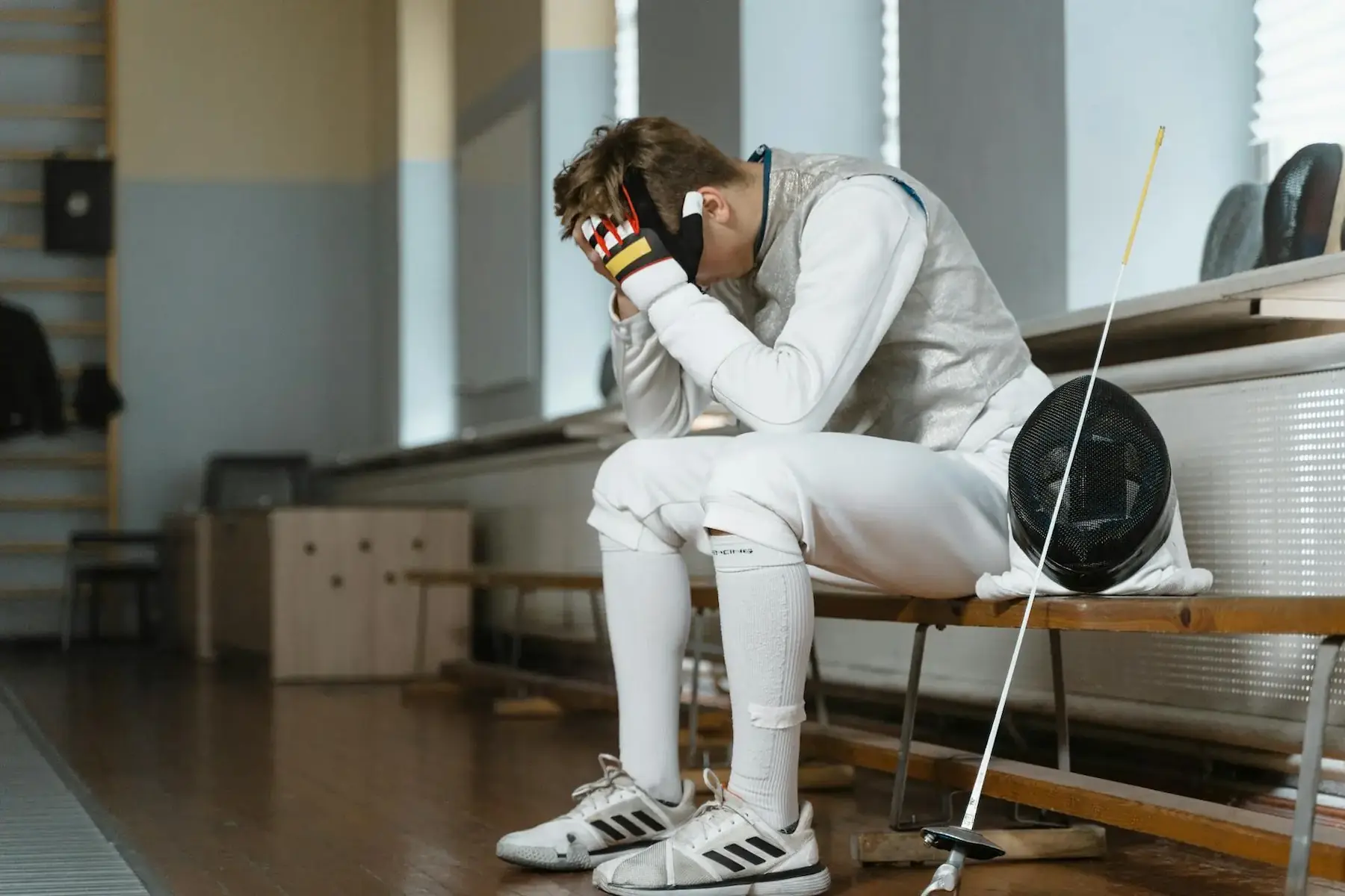 a frustrated fencer sitting on a bench with their head in their hands