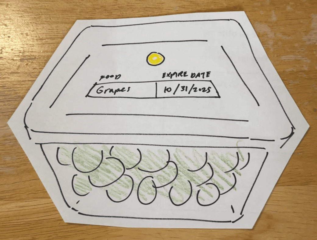 Hexagonal takeout container with a labeled lid, featuring drawn grapes inside.