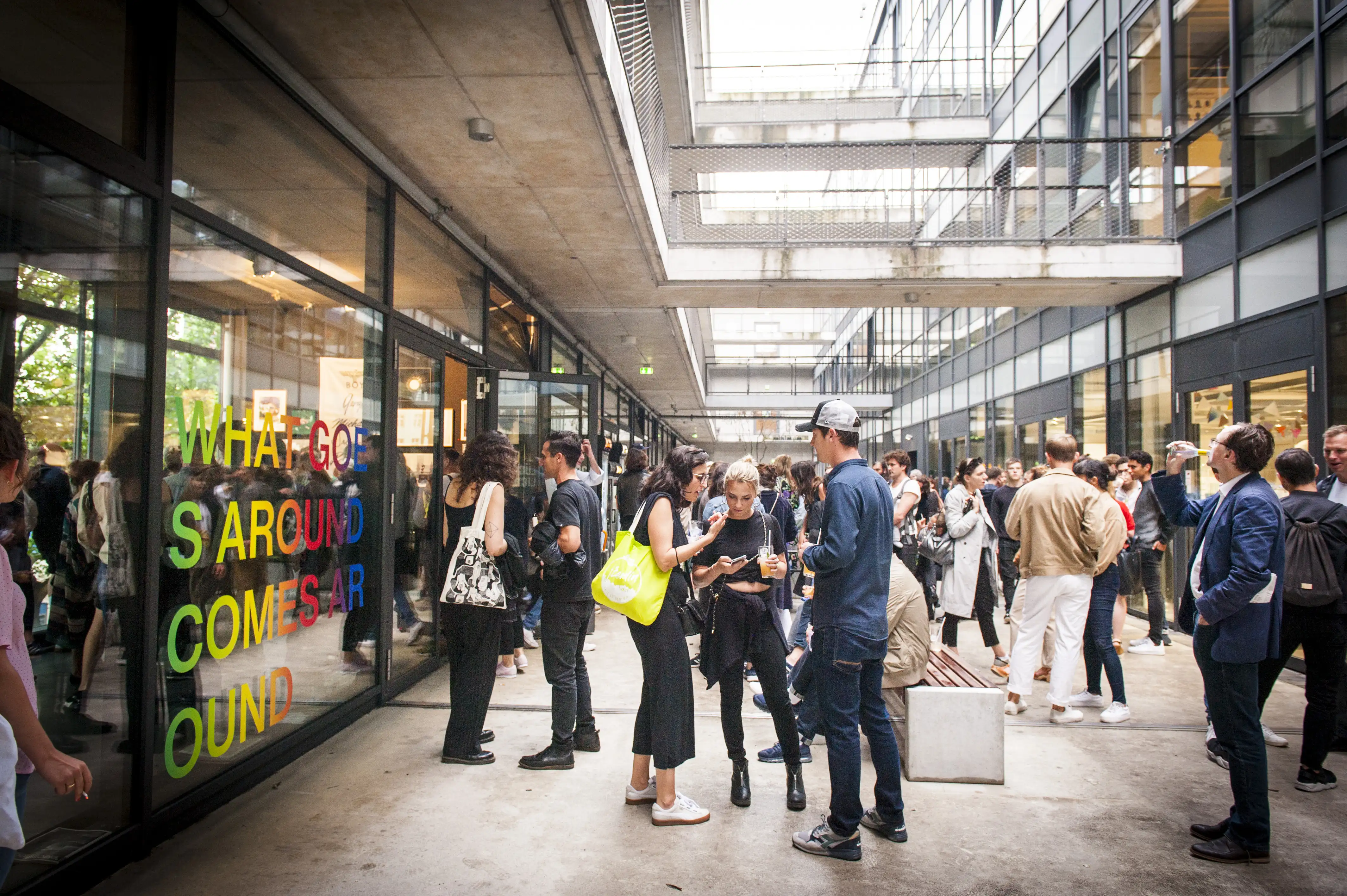 Crowd of visitors outside the STUDIOLO gallery in a modern courtyard, with the colorful window lettering on the left.