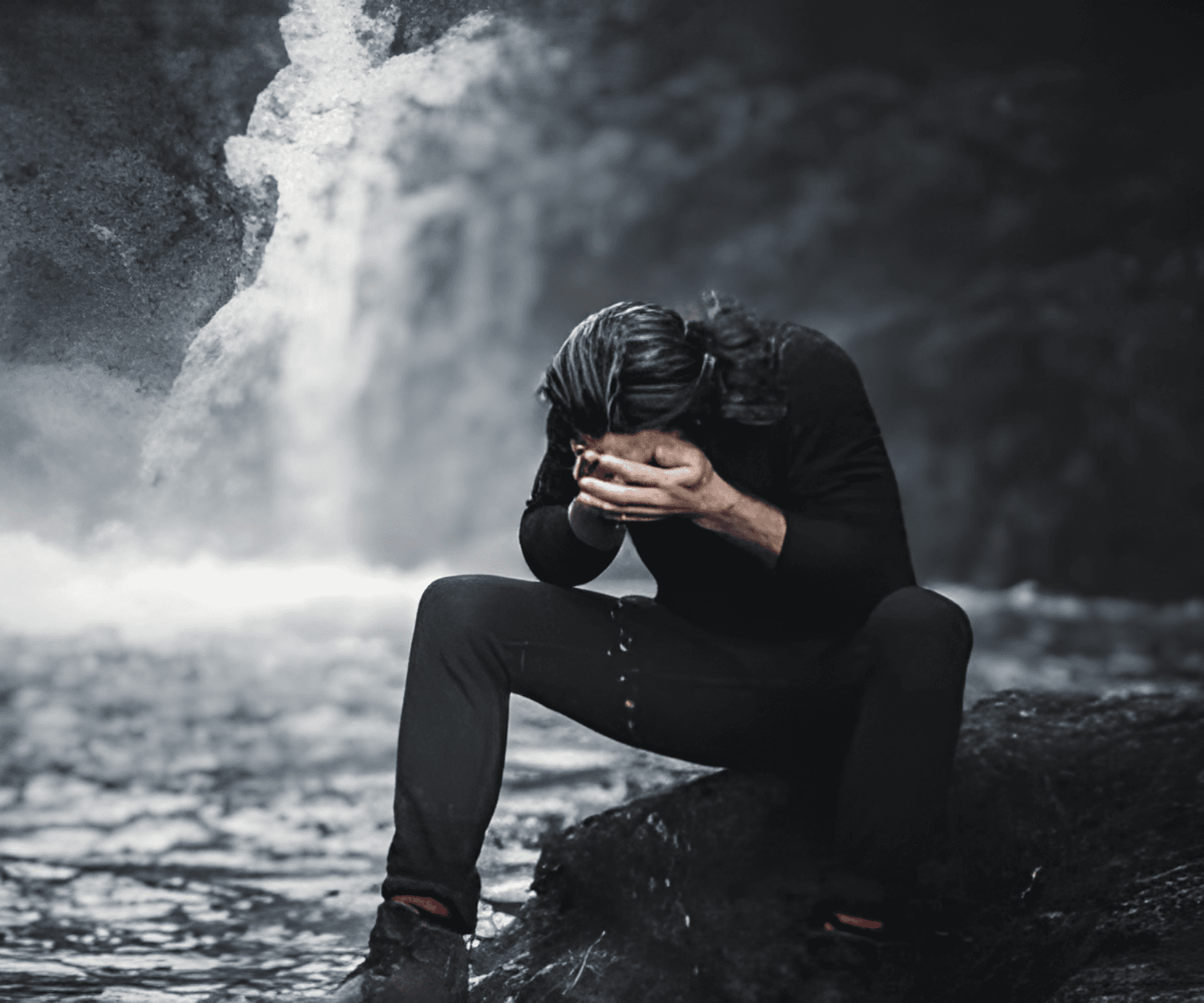 Man sitting by a waterfall with head in hands.