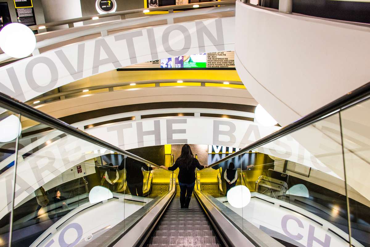 A wide shot from an escalator looking down into a modern train station concourse with white text overlaid on the frame.