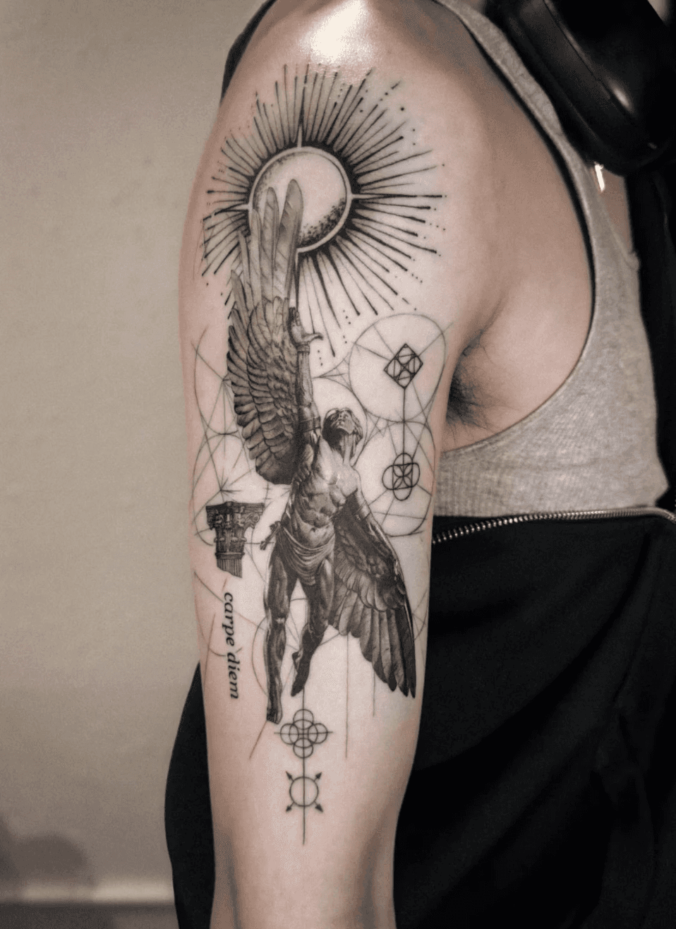 Winged figure tattoo with sun and geometric details.
