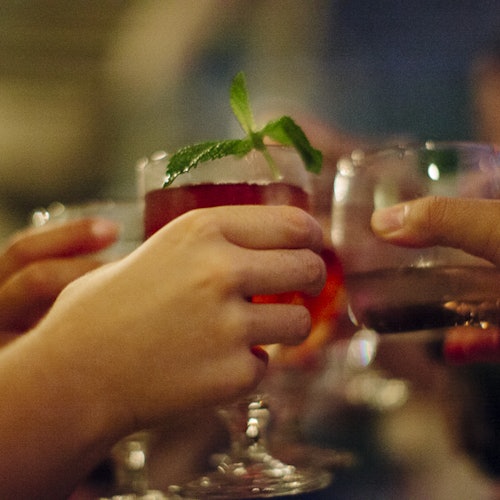 几只手举着饮料杯庆祝干杯；一杯饮料上有薄荷装饰。