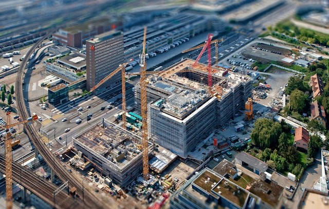 Aerial view of an active urban construction site with red cranes and multi-story buildings under development