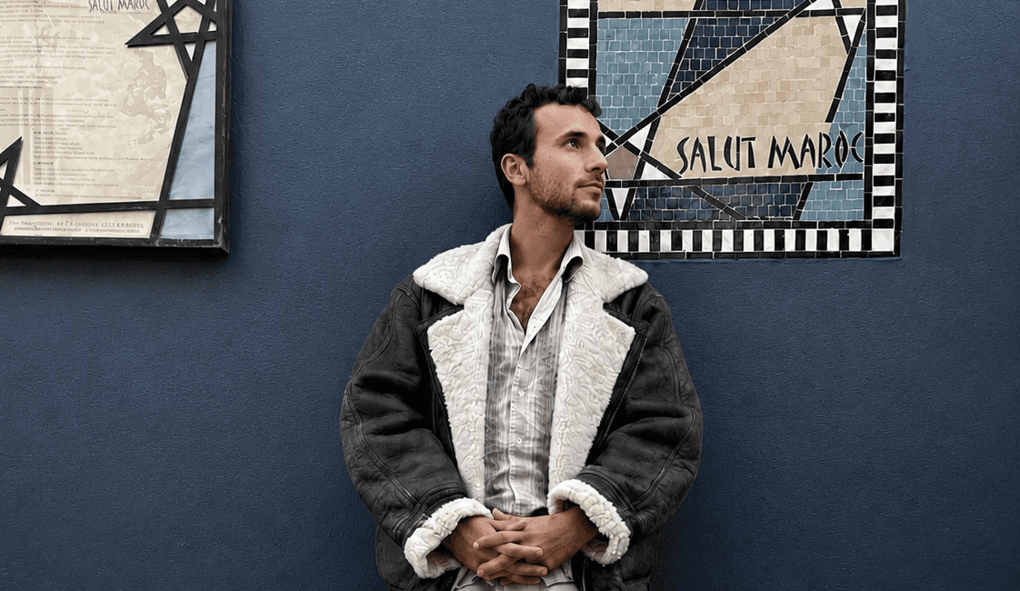 Roméo Morghati standing against a blue wall with a Salut Maroc mosaic panel