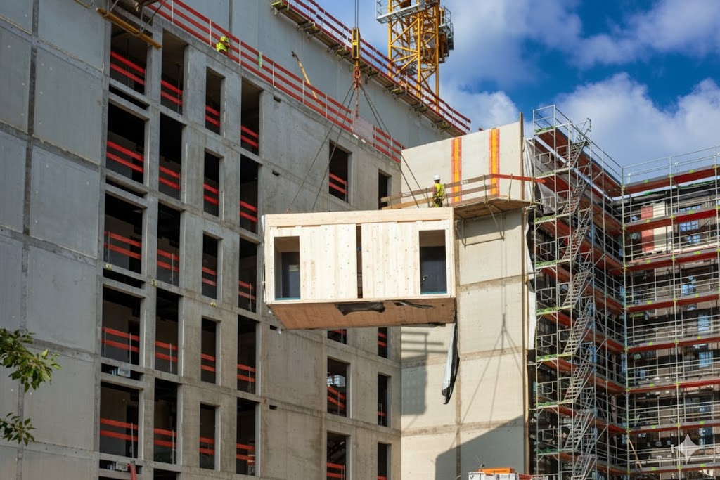 Baukran hebt ein vorgefertigtes Raummodul in den Rohbau eines Hochhauses – Zeitsparende und effiziente Modulare Konstruktion.