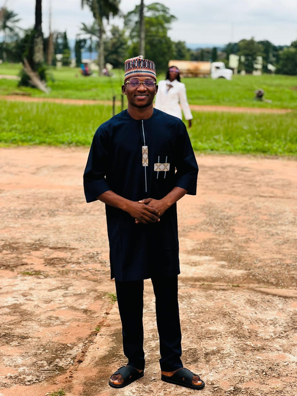 Smiling man in a dark suit and tie stands in a well-lit room, exuding confidence and professionalism. Background features blurred office decor.