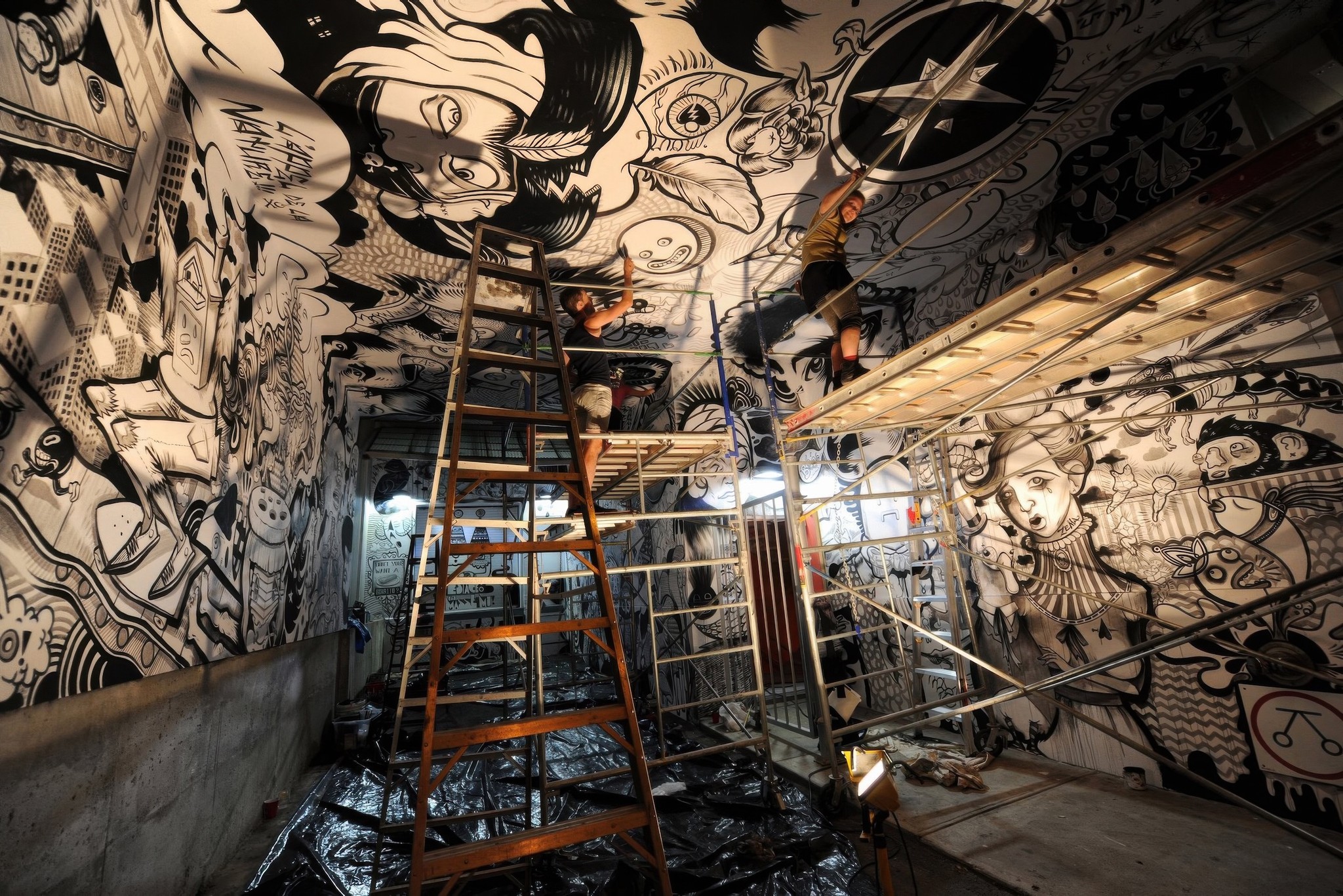 A long room wrapped floor to ceiling in black-and-white drawings, ladders and scaffolding standing at its centre.