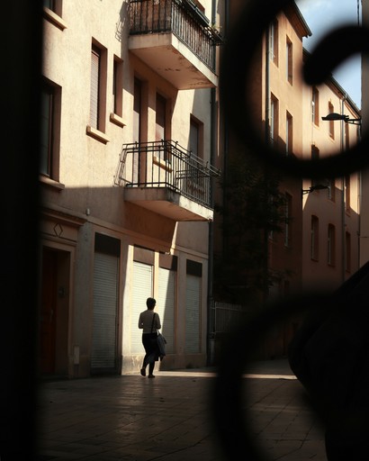 A person walks down a sunlit street.