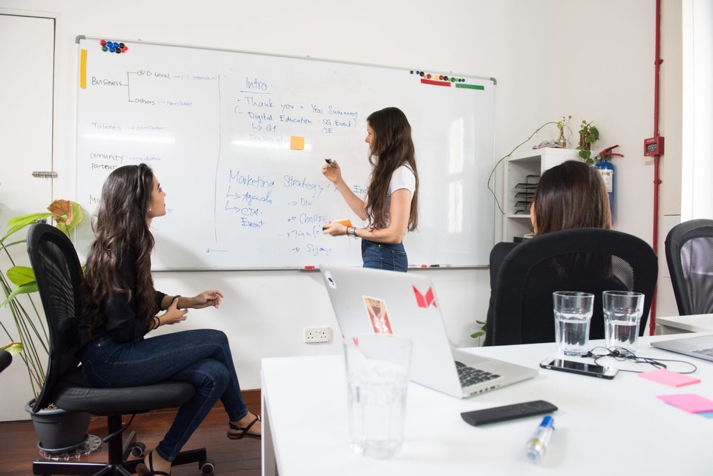 Team collaboration in modern office, women discussing strategy at whiteboard.