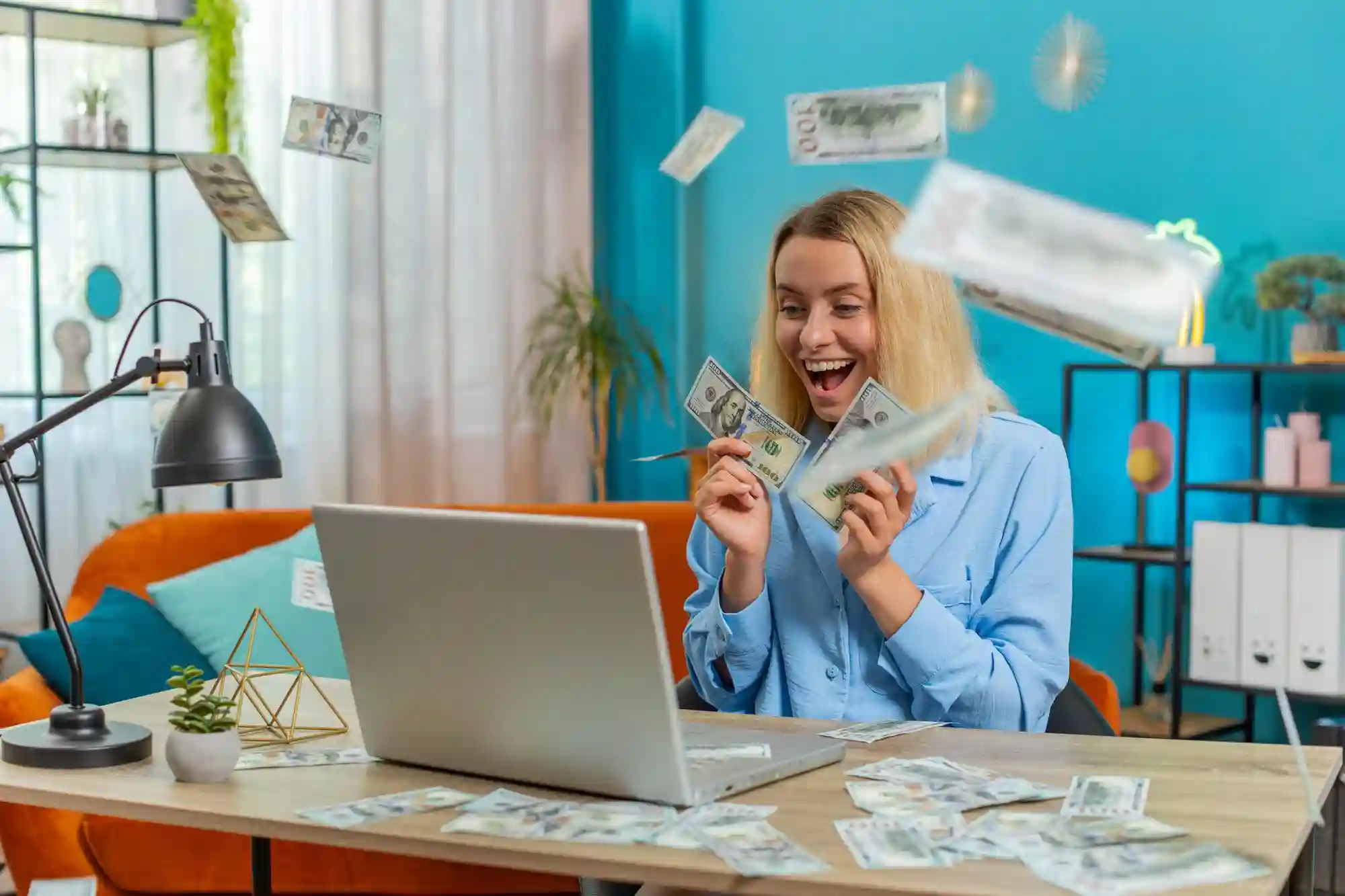 Young woman celebrating with cash flying around her and a laptop.