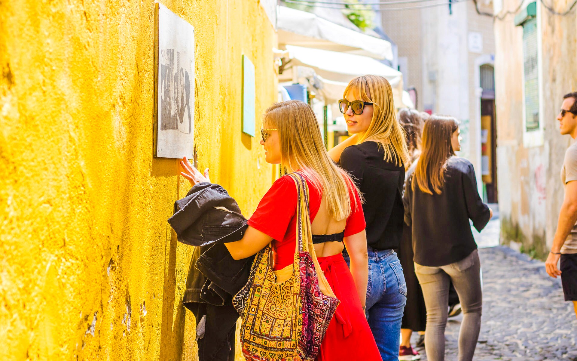 Woman observing Camilla Watson's renowned portraits in Lisbon alleyway.