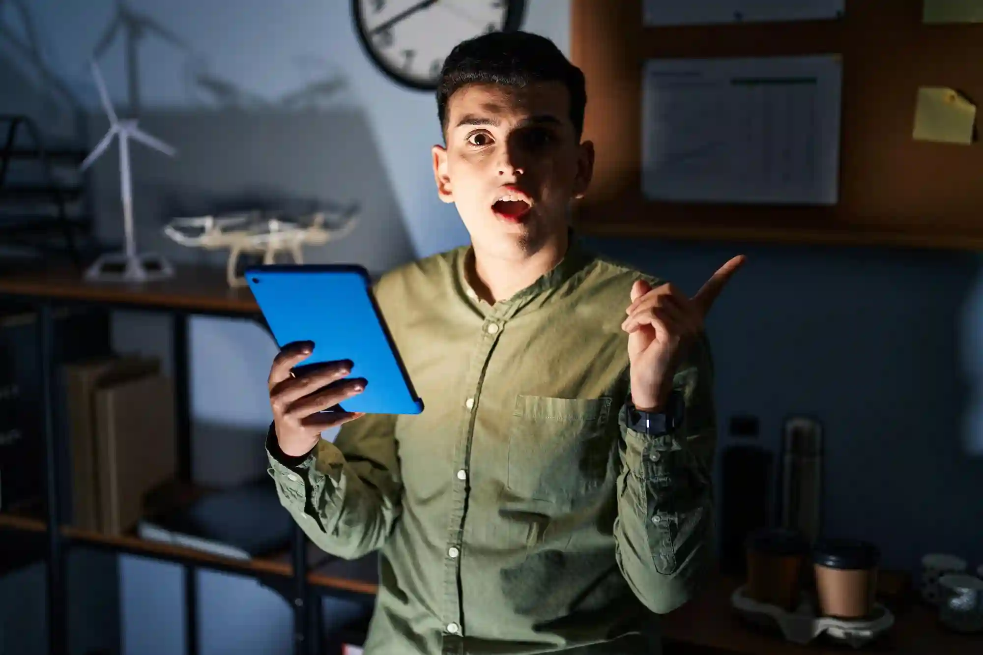 Man holding a tablet, speaking passionately while pointing, in an office setting with wind turbine models, suggesting a discussion about sustainable energy projects.