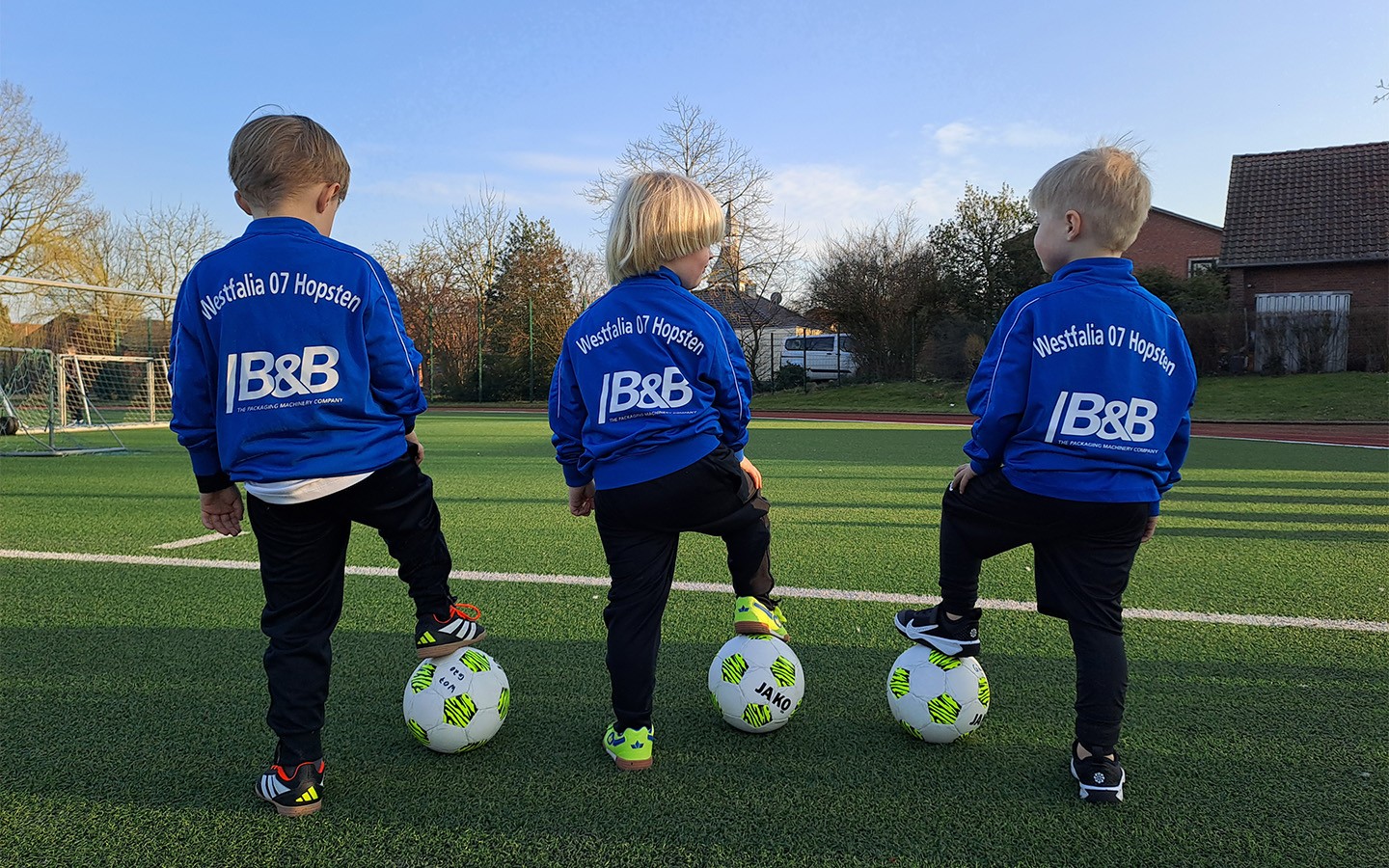 Drei kleine Fußballspieler mit Ball auf dem Rasen. Kinder im blauen Trikot von Borussia 67 Hopsen.