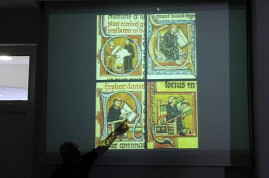 A photo of a man showing some century old drawings on a screen projector.