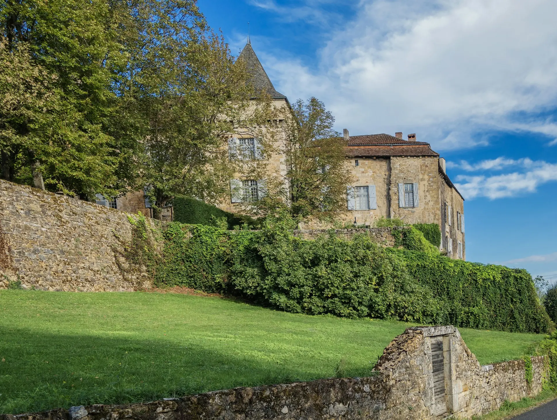 Traditional stone house with a green lawn and stone wall in the Célé Valley, Lot, France, perfect for sustainable real estate investment.