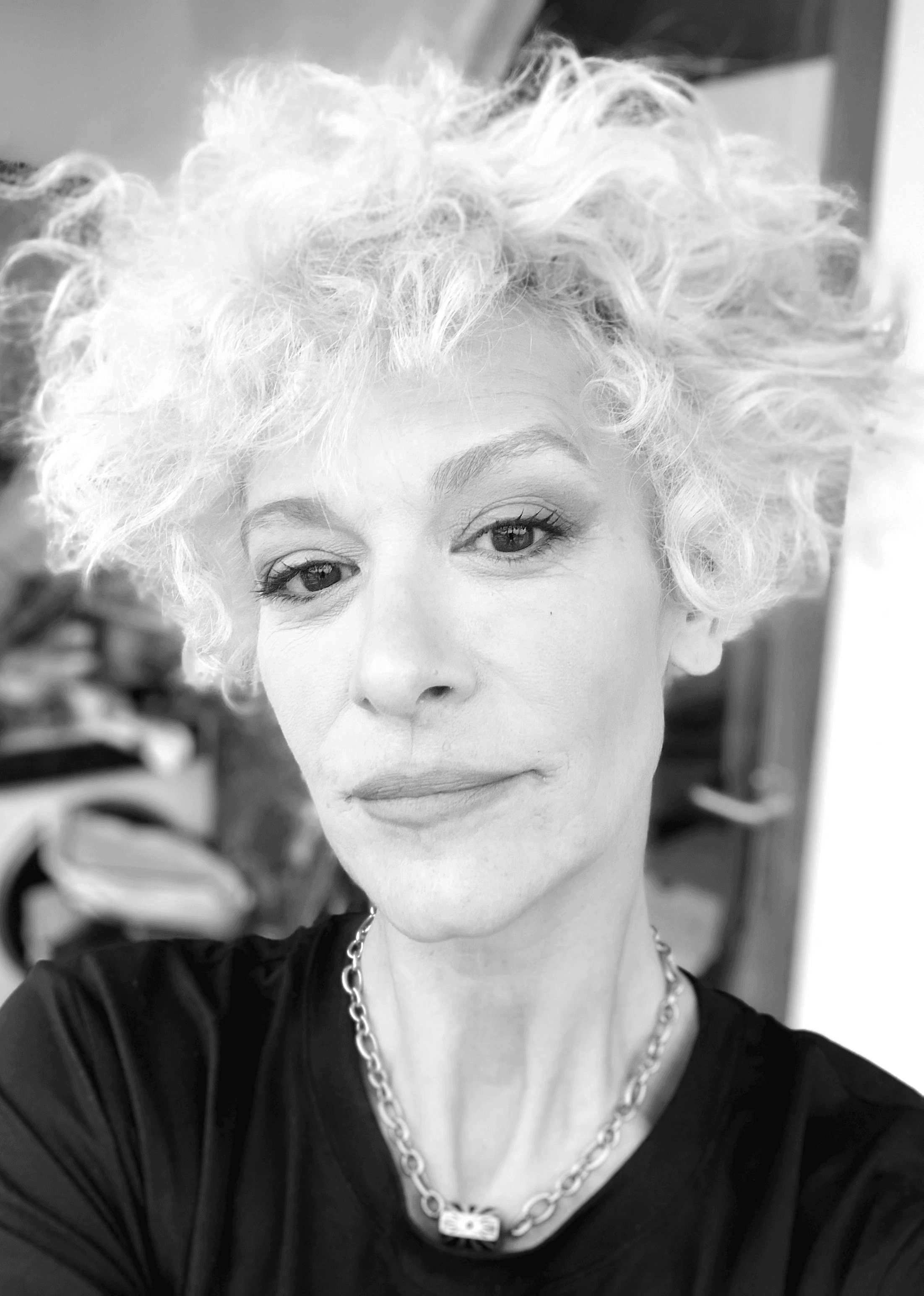 Una persona con una camiseta negra y pantalones de color claro está de pie en la cima rocosa de una montaña al atardecer, sosteniendo una cámara frente a su cara para tomar una foto. Un mar de nubes se extiende detrás de ellos, iluminado por la luz dorada del sol poniente.