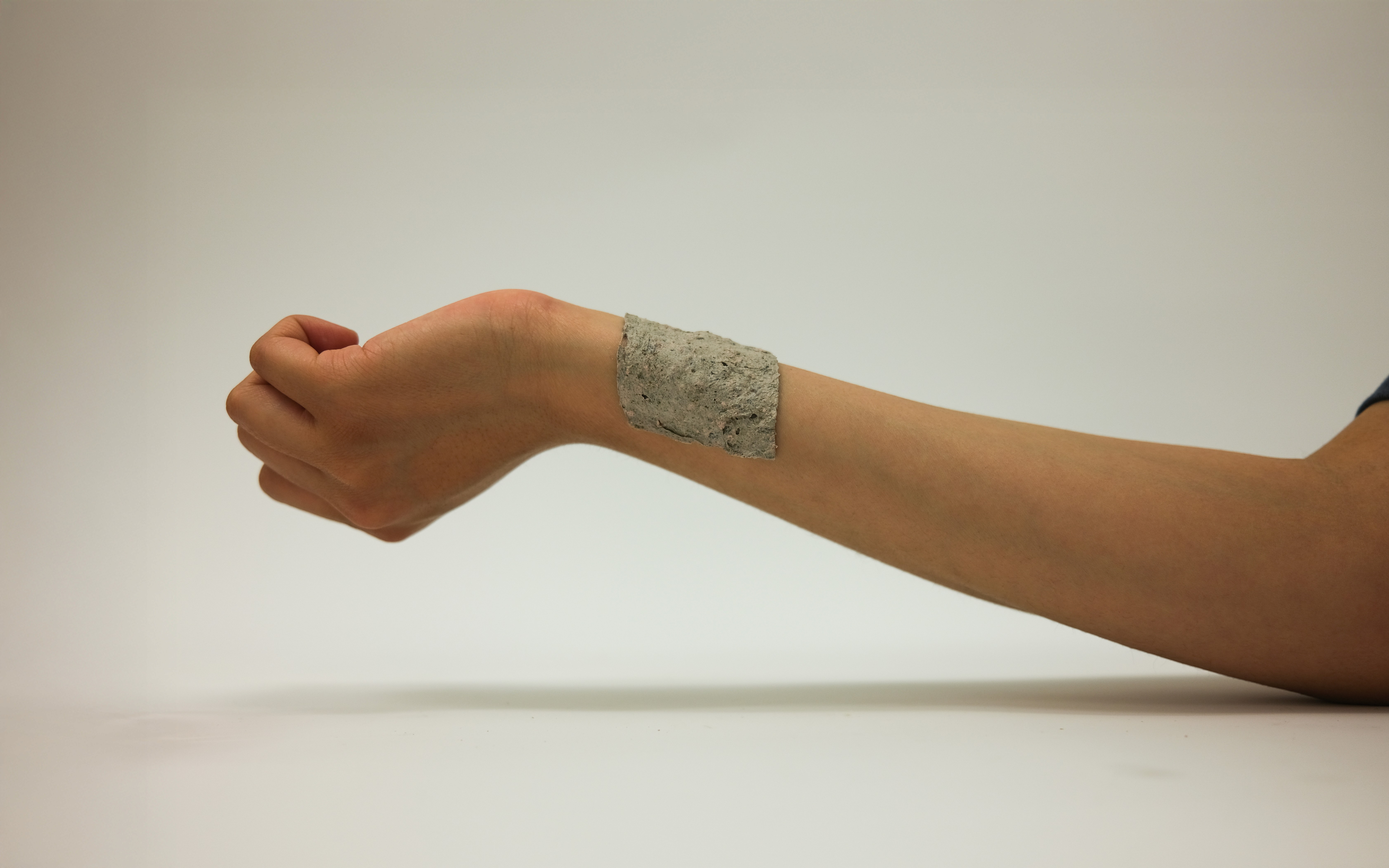Outstretched arm wearing a poultice patch made from a textured, organic material applied to the inner forearm. Set against a plain background, the image highlights the final prototype developed in this project.