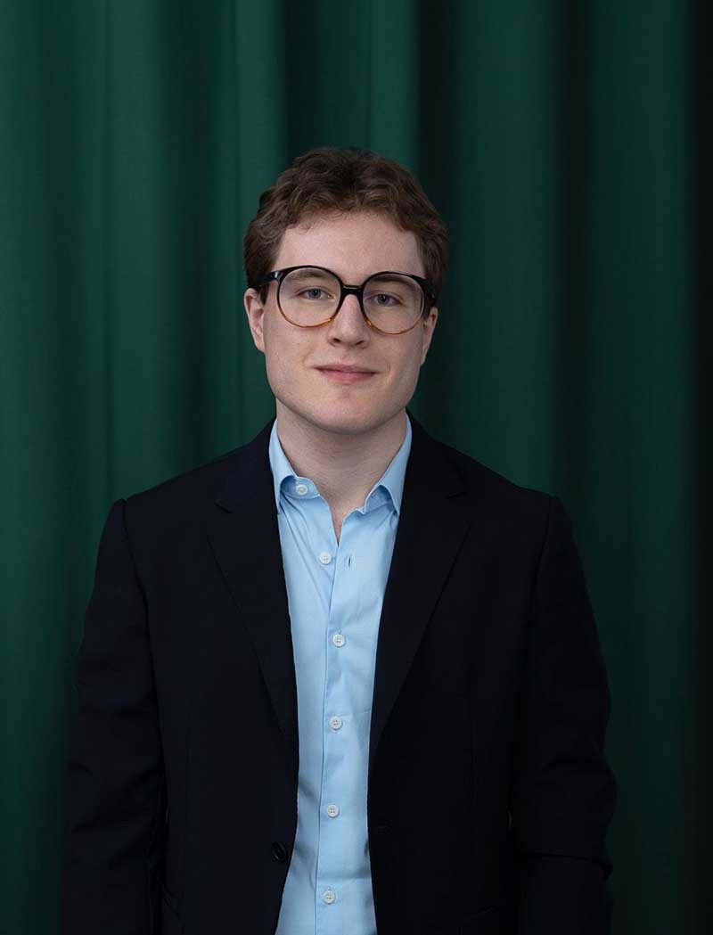 Elke Stoll-Weber mit kurzen dunklen Haaren und schwarzem Hemd lehnt entspannt an einem Holztisch in einem hellen Raum